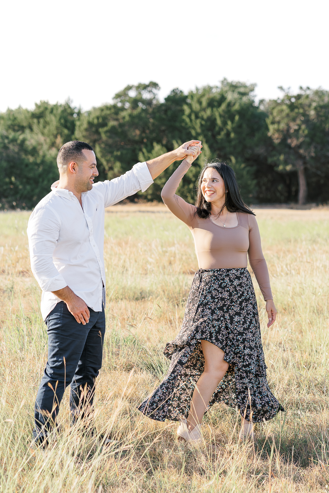 A couple is dancing in a field of tall grass, beautifully captured by an Austin family photographer. The wife looks at her husband smiling while her husband spins her.