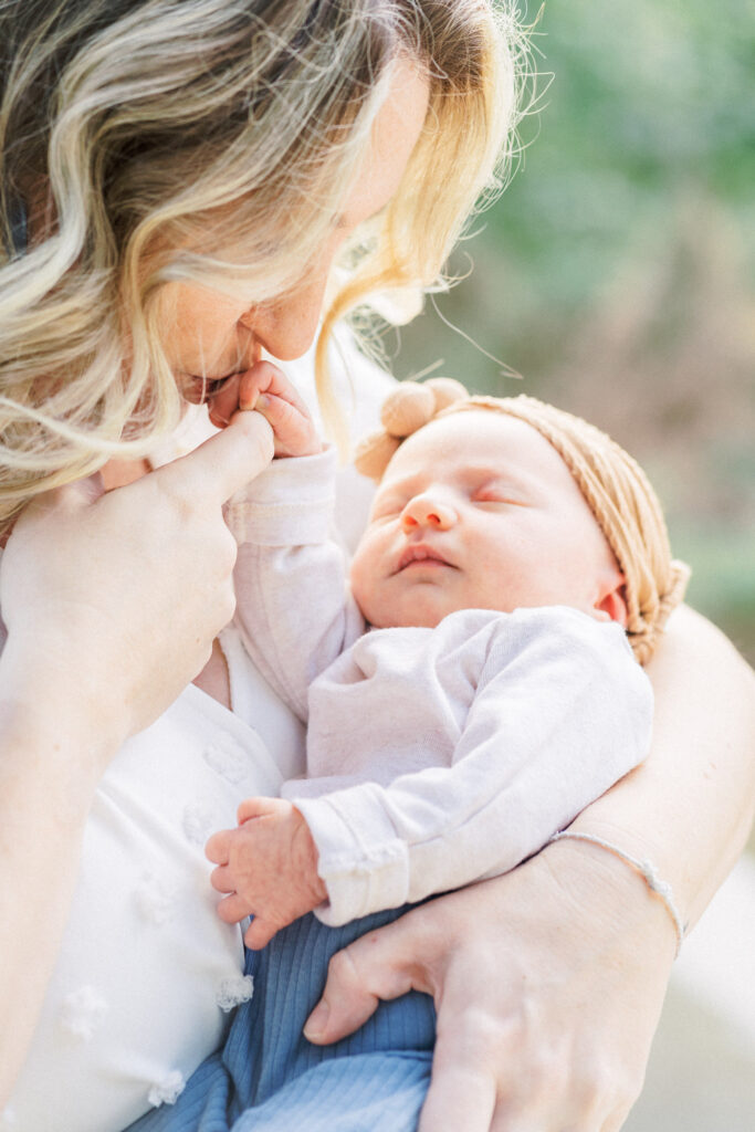 A mother holds her newborn baby and kisses her baby's hand in a tender moment captured by an Austin Newborn Photographer.