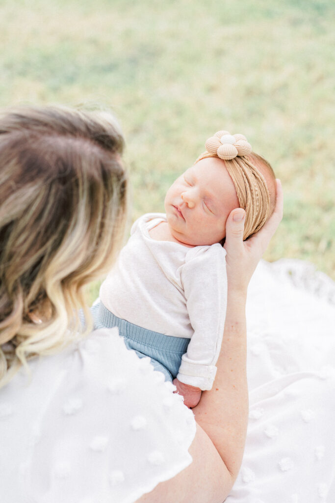 A newborn baby girl is held by her mother and sleeps peacefully during an outdoor newborn photo session captured by an Austin Newborn Photographer.