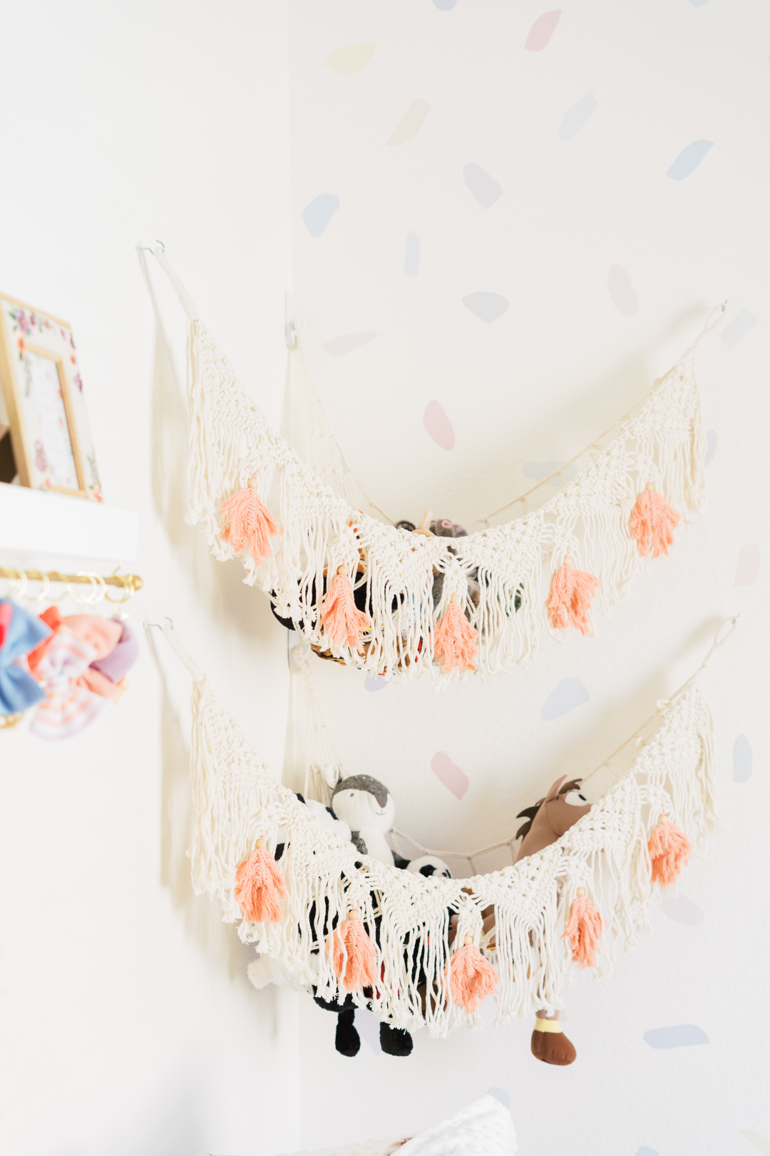 Detail shot in a baby girl's nursery of hanging stuffy holders. The wall paper has pastel confetti as an accent. 