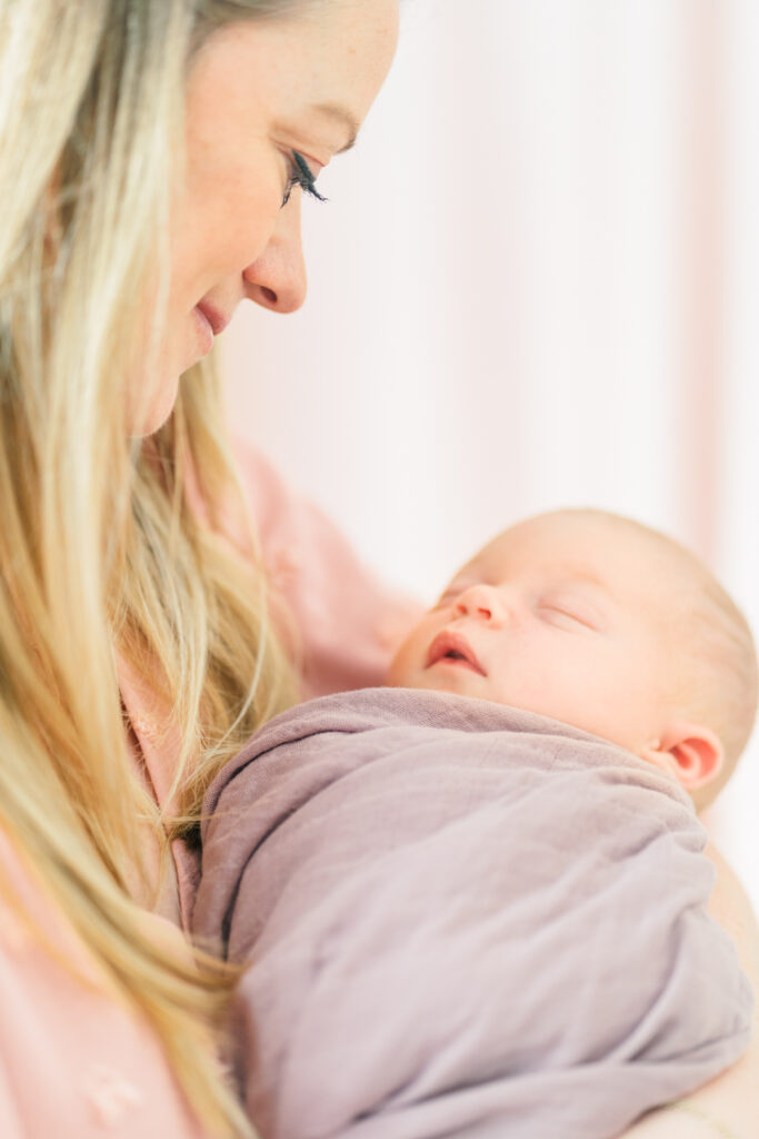 A mother holds her newborn baby girl in her arms while looking down at her and smiling in a tender moment photographed by an Austin newborn photographer.