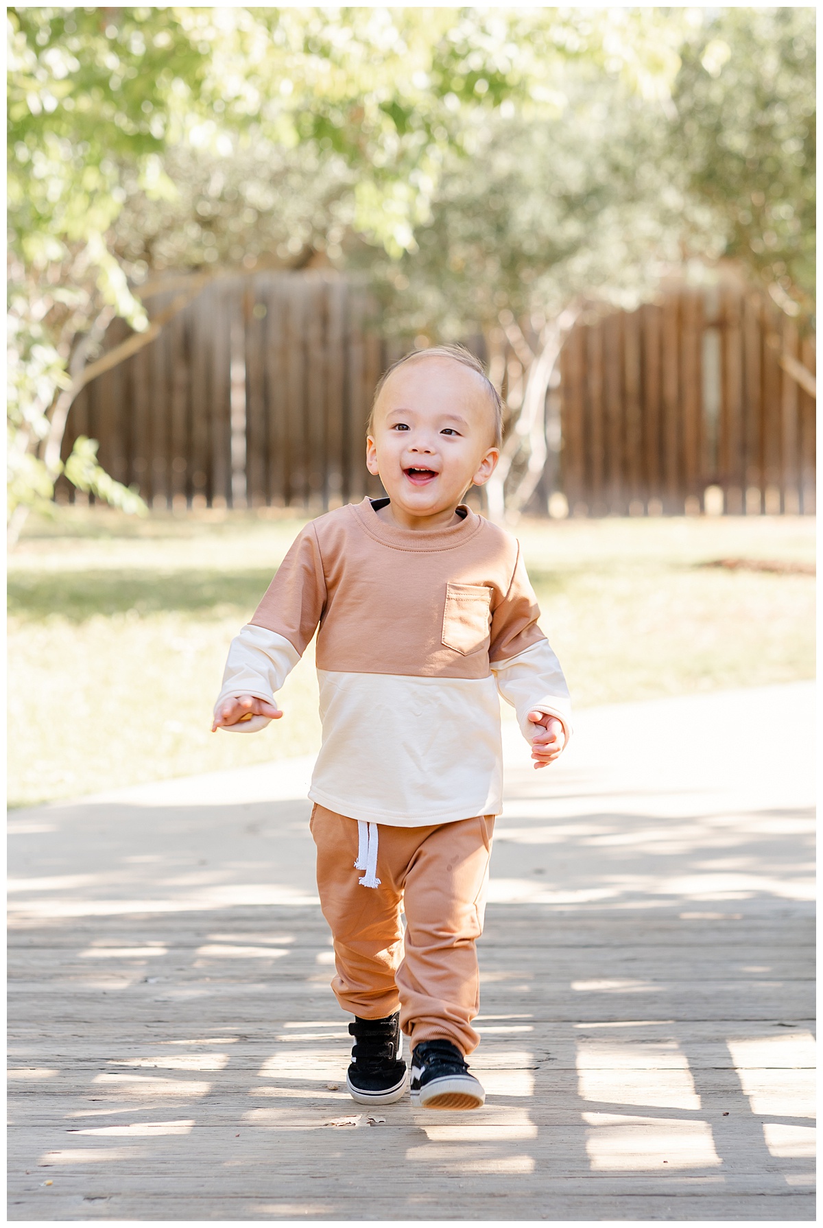 Austin Moms | A baby boy dressed in an orange and cream outfit runs on a bridge at Katherine Fleischer Park. He looks at his mother and smiles.