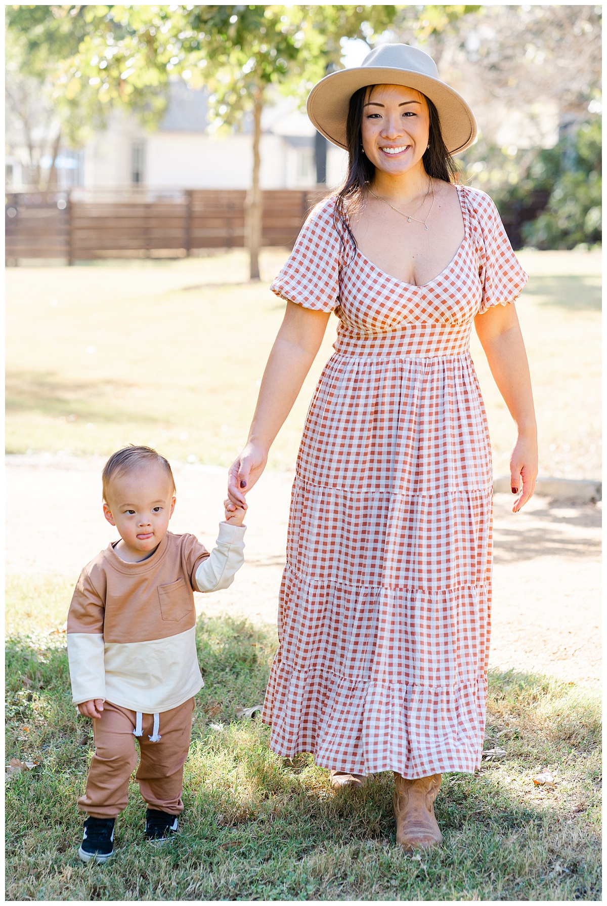 Austin Moms | A mother dressed in a burnt orange gingham midi dress holds her baby boy's hand. They walk in a park during this mommy and me photoshoot in Austin, TX. 
