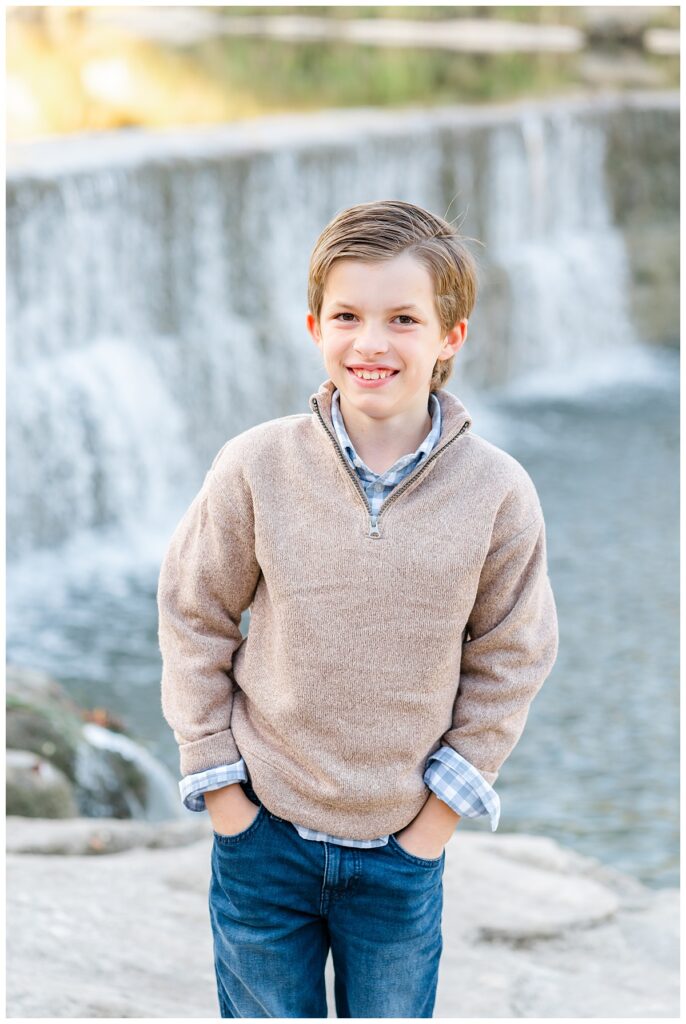 A young boy poses in front of a waterfall in this shot taken at Blue Hole Park by a Georgetown Texas Photographer.