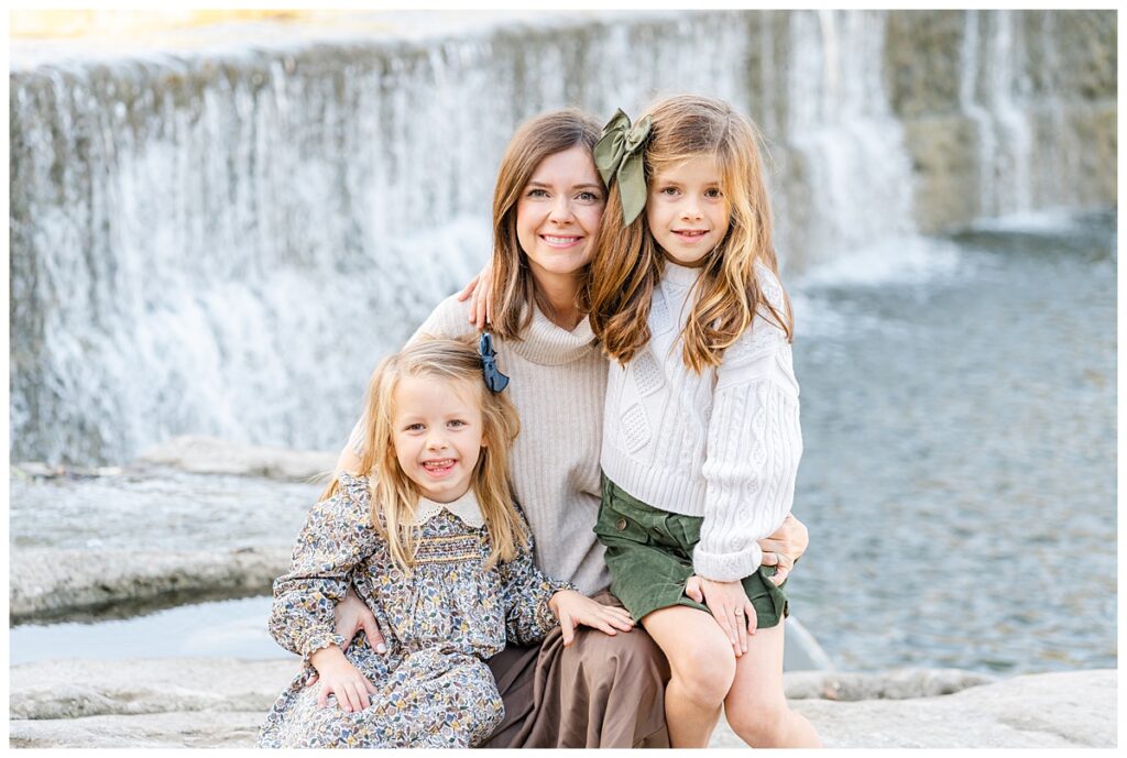 A mother and her two daughters sit in front of a waterfall at Blue Hole Park. They all look at the camera and smile in this posed photo taken by a Georgetown Texas Photographer.