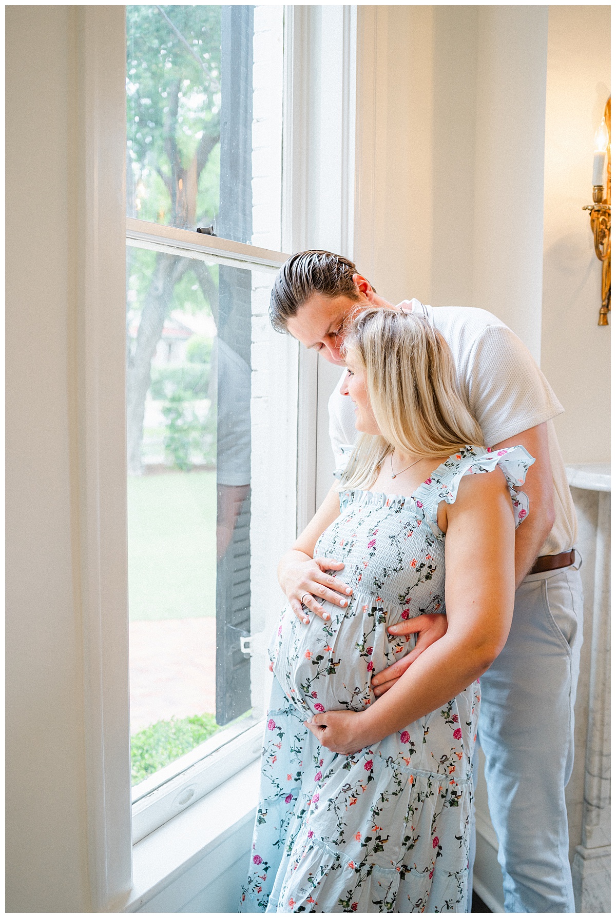 A husband and wife look out a window at the Woodbine Mansion in Round Rock during their photo session with an Austin Maternity Photographer.