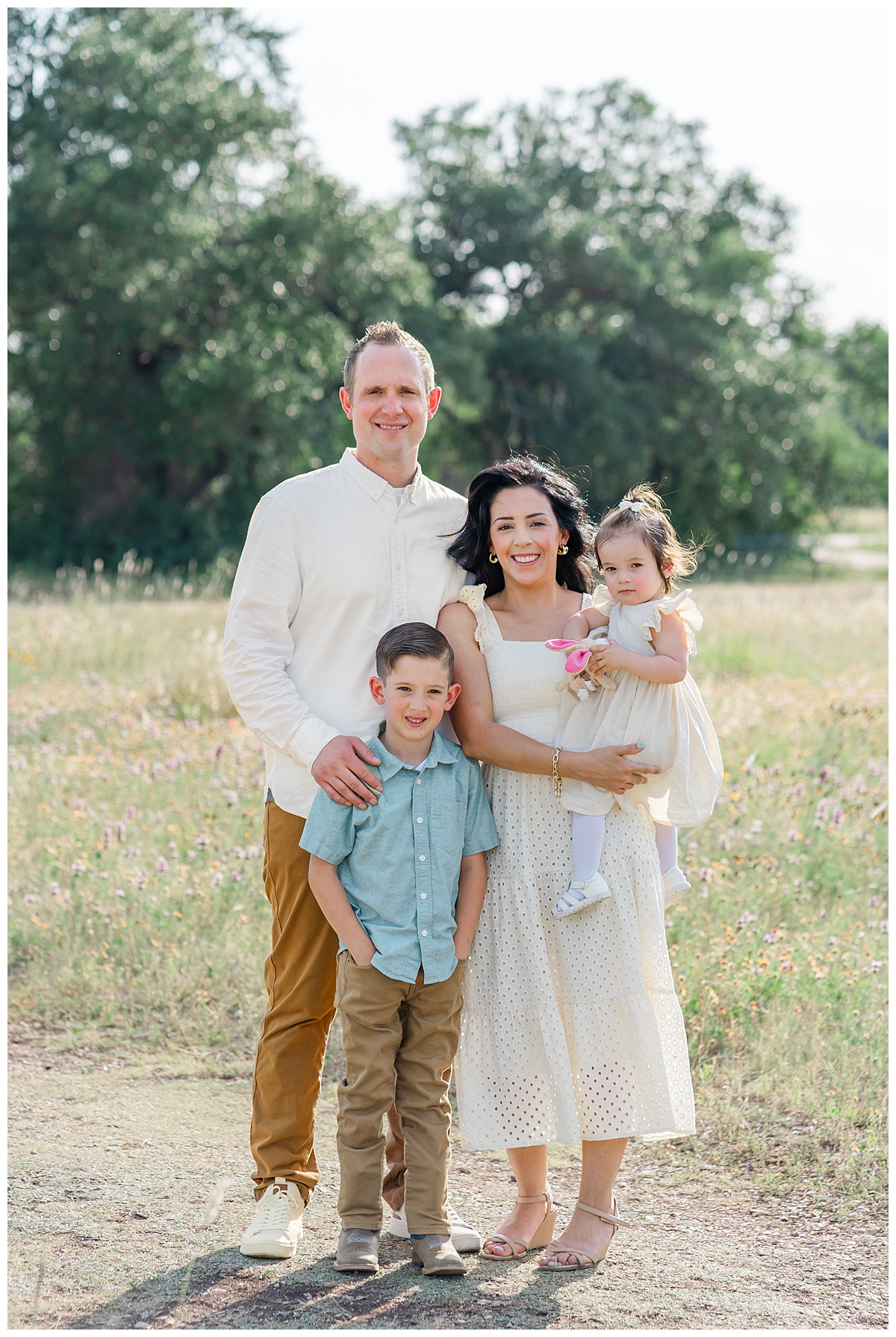 A family of four stands on a sandy path at Brushy Creek Lake Park. They pose and smile at the camera for this family portrait captured by a Cedar Park Photographer.