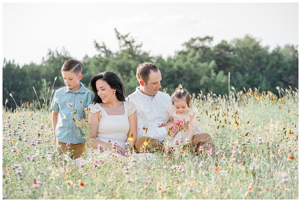 family of four sits in a field of wildflowers for their family photos, captured by a Cedar Park Family Photographer.