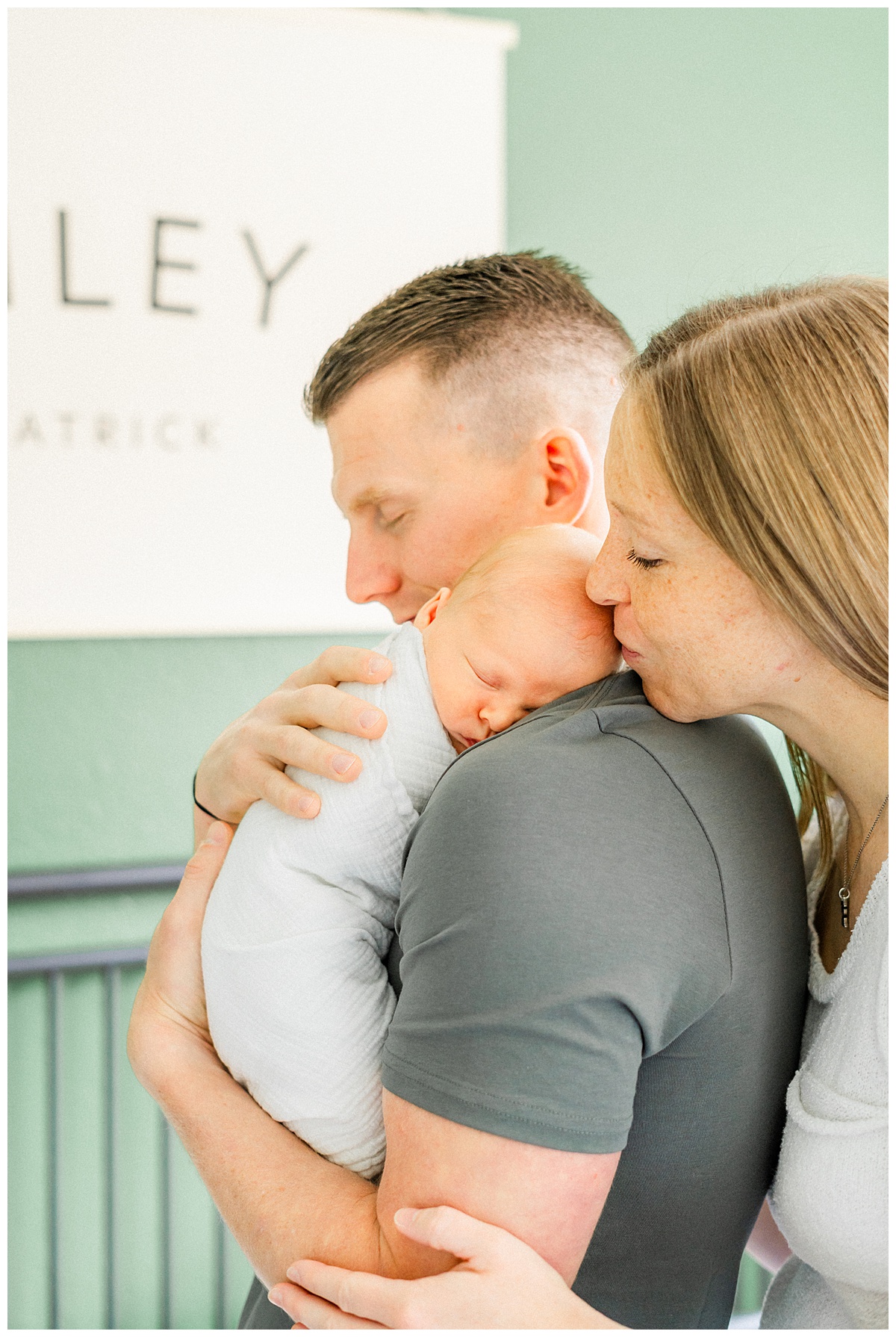 A newborn baby rests on his father's shoulder while his mother kisses him on the head in this candid shot taken by a Georgetown, TX in-home newborn photographer.