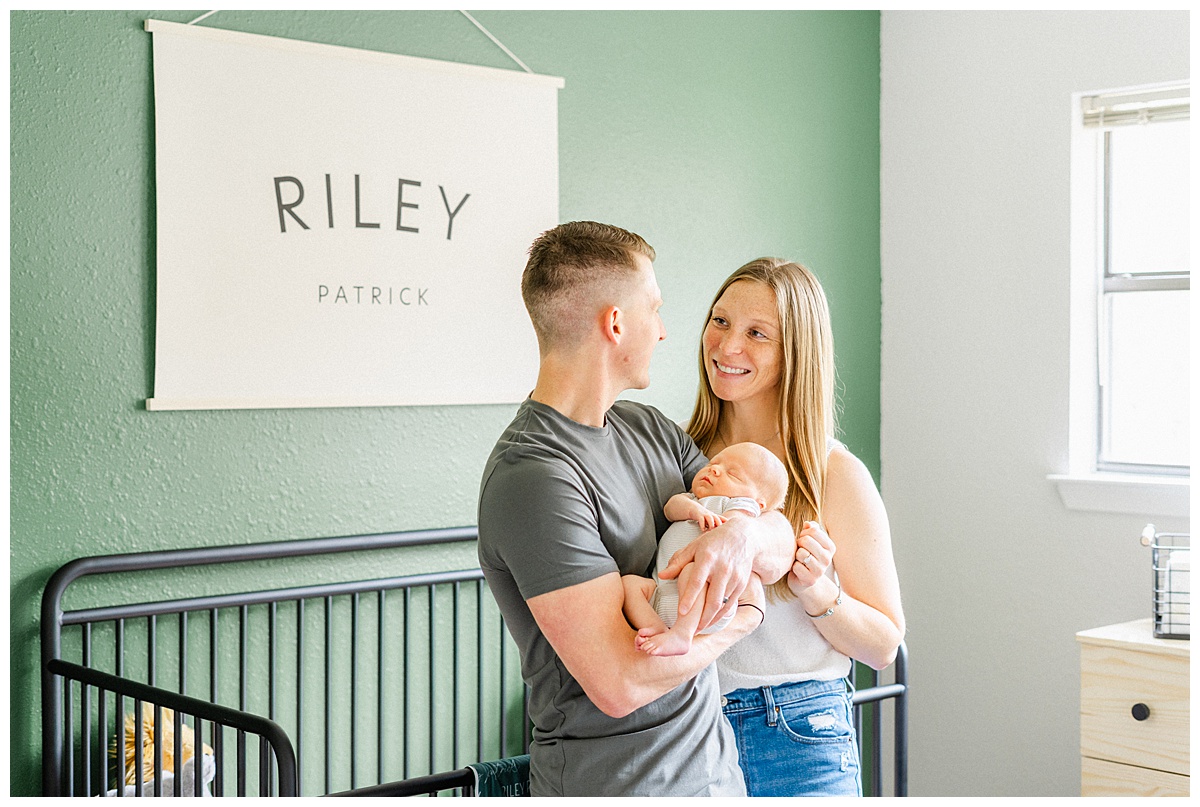 A father holds his baby in the nursery in their Georgetown, TX home while looking at his wife smiling.