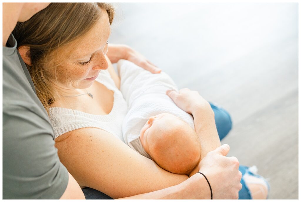 A mother and father sits on the floor of their Georgetown, TX home. They both look down at their newborn baby.