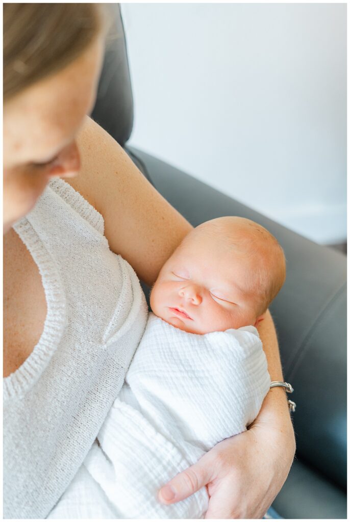 A newborn is swaddled in a white blanket and sleeps in his mother's arms during his photoshoot in his Georgetown, TX home.