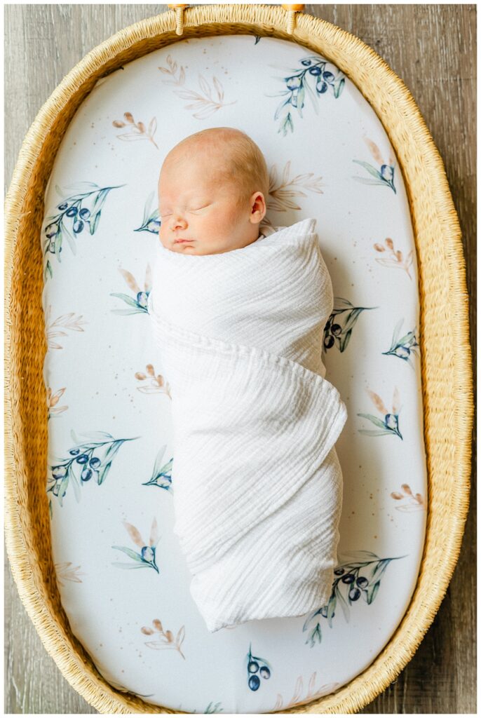 a baby lays in a bassinet swaddled in a white blanket, captured by a Georgetown, TX newborn photographer.