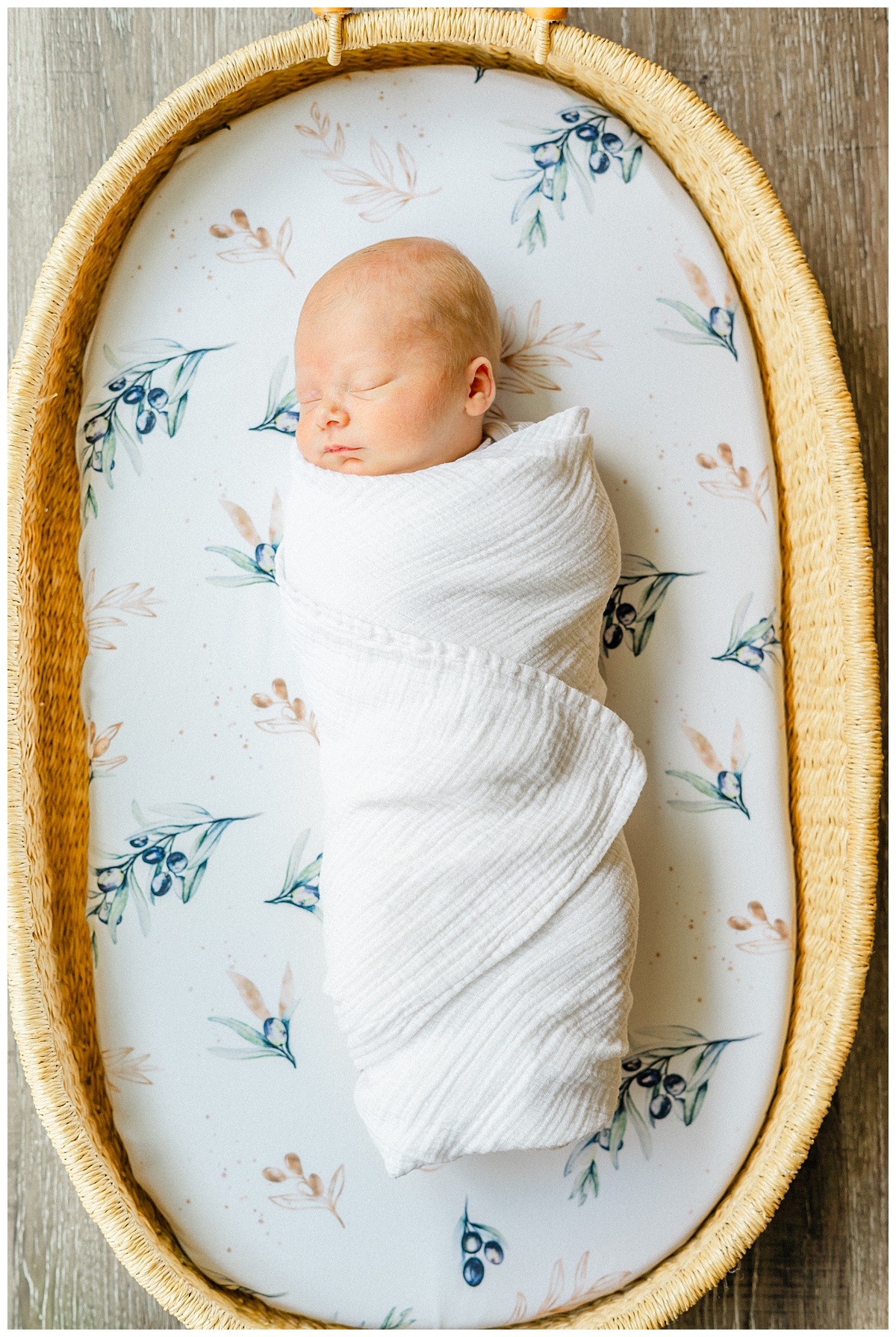 A newborn lays in a moses basket, swaddled in a white blanket.
