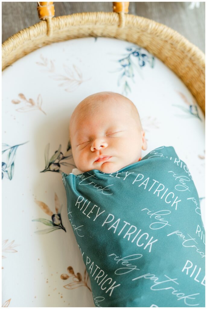 A newborn baby wrapped in a dark green blank lays in a basket in his Georgetown, TX home.