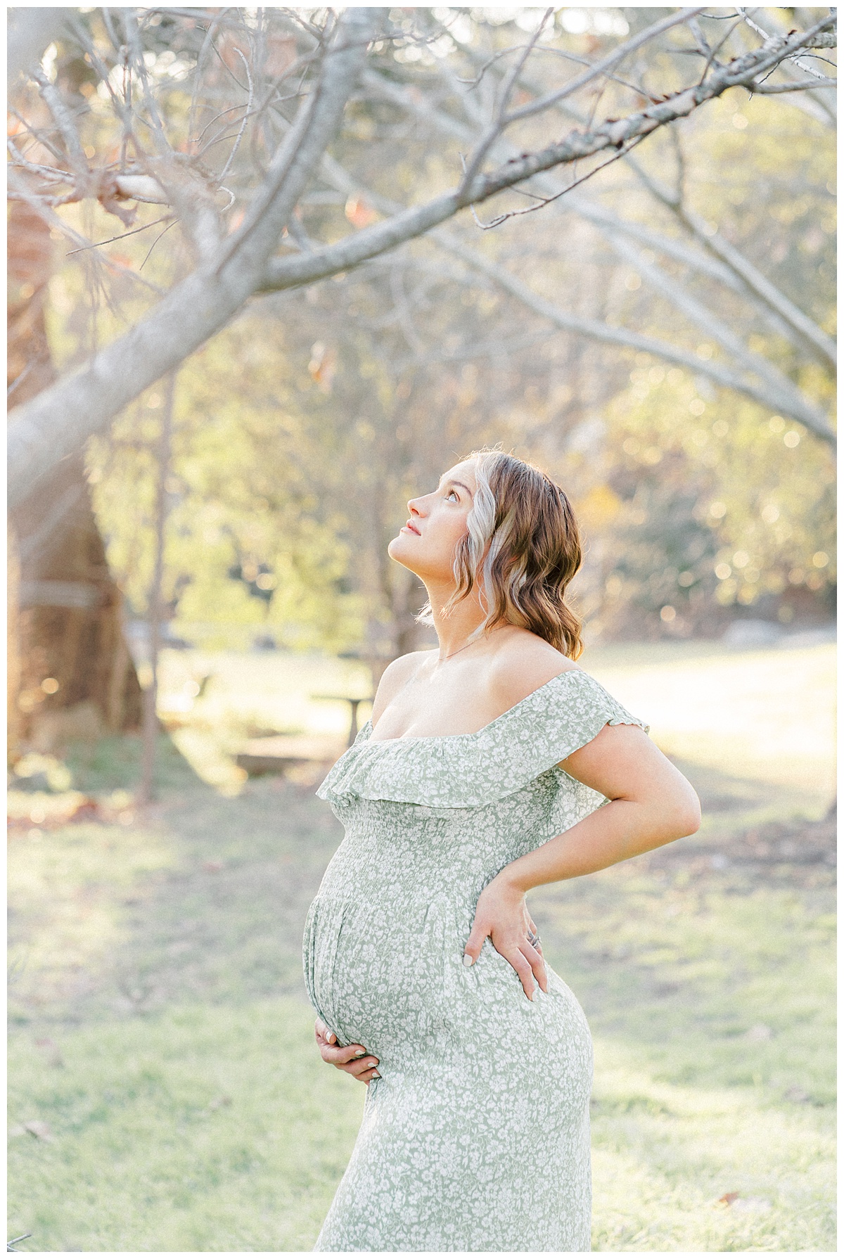 A pregnant mother stands under a tree at Bull Creek District Park. She looks up in the sky.