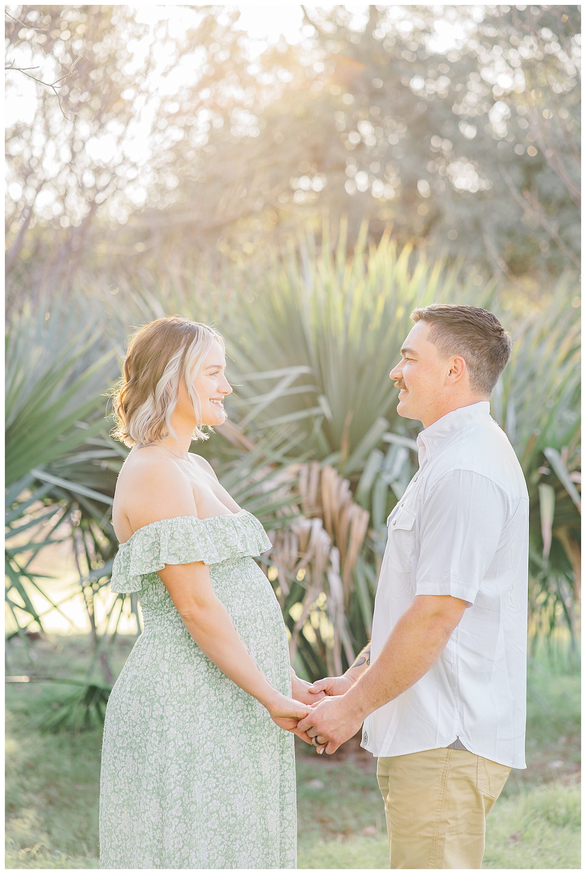 A couple stands facing each other at Bull creek District Park and smile at each other. The wife is pregnant.