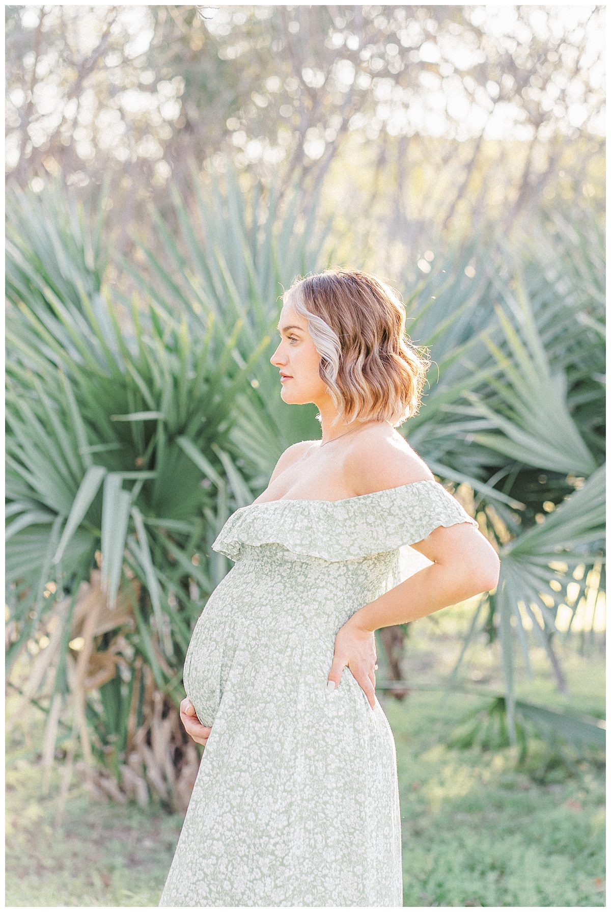 A pregnant mother stands in front of a palm tree at Bull Creek District Park for her maternity photos in Austin, TX. She is dressed in a long green dress.