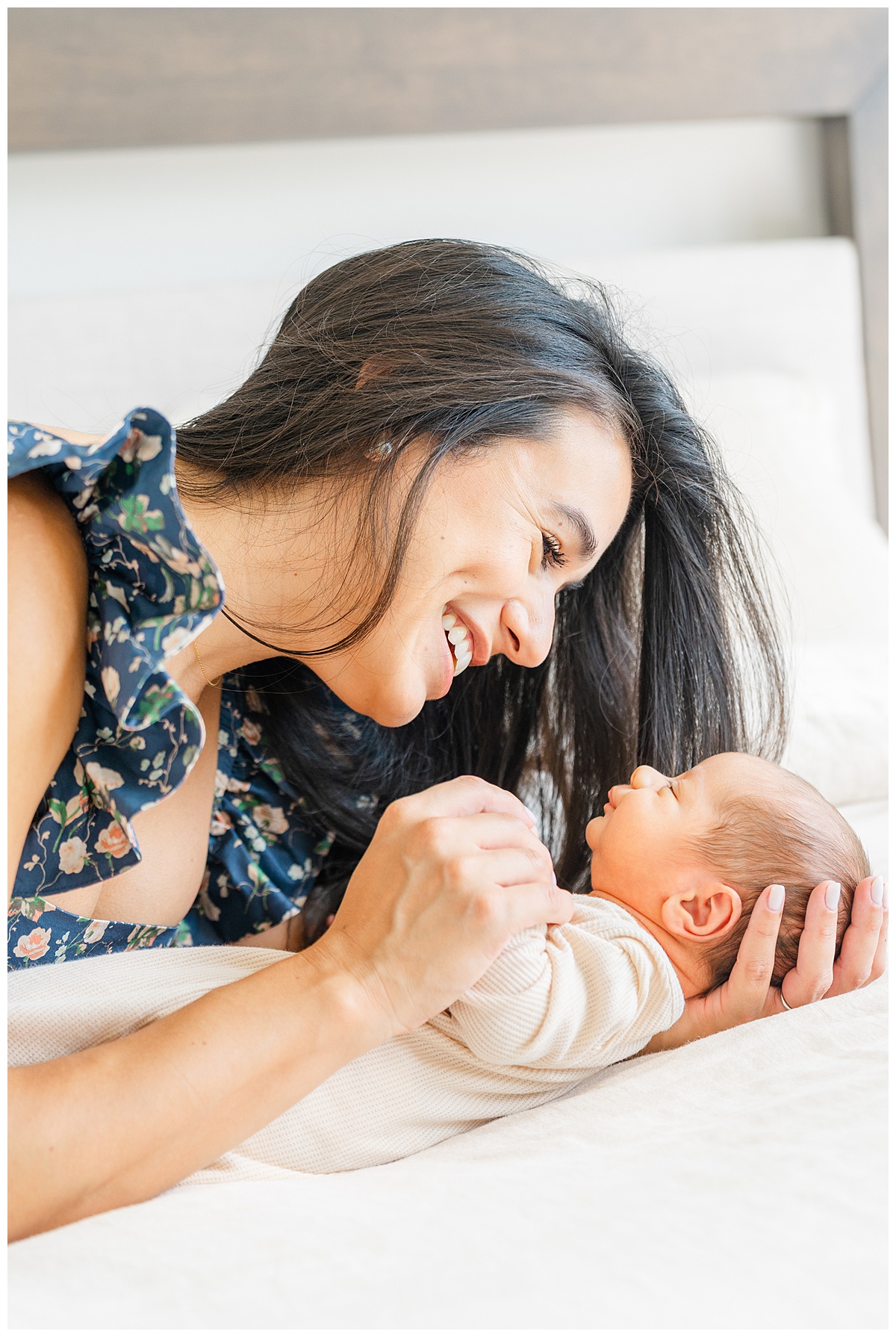 A mother lays on a bed facing her newborn baby. She smiles at her baby in this candid photo taken by a Leander Photographer.