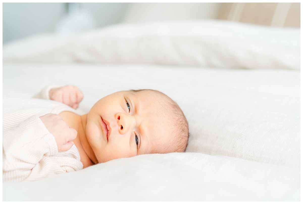 a newborn baby lays on a beige bedspread. He is awake and looks at the camera of his Leander Newborn Photographer.