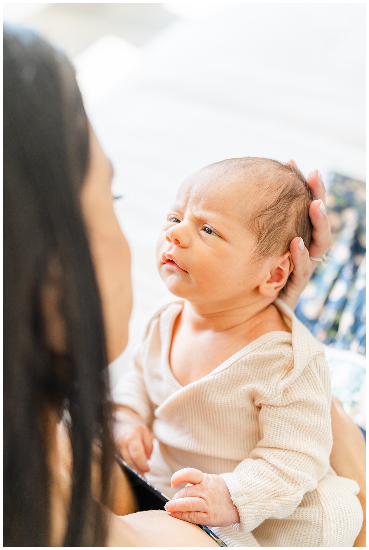 A mother holds her newborn baby facing her. The baby has his eyes opened and looks up at his mother in this tender moment captured by a Leander Photographer.