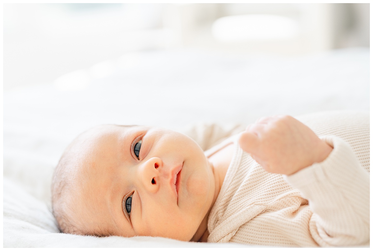 Newborn baby laying on a bed with his eyes open, captured by a Leander Photographer.
