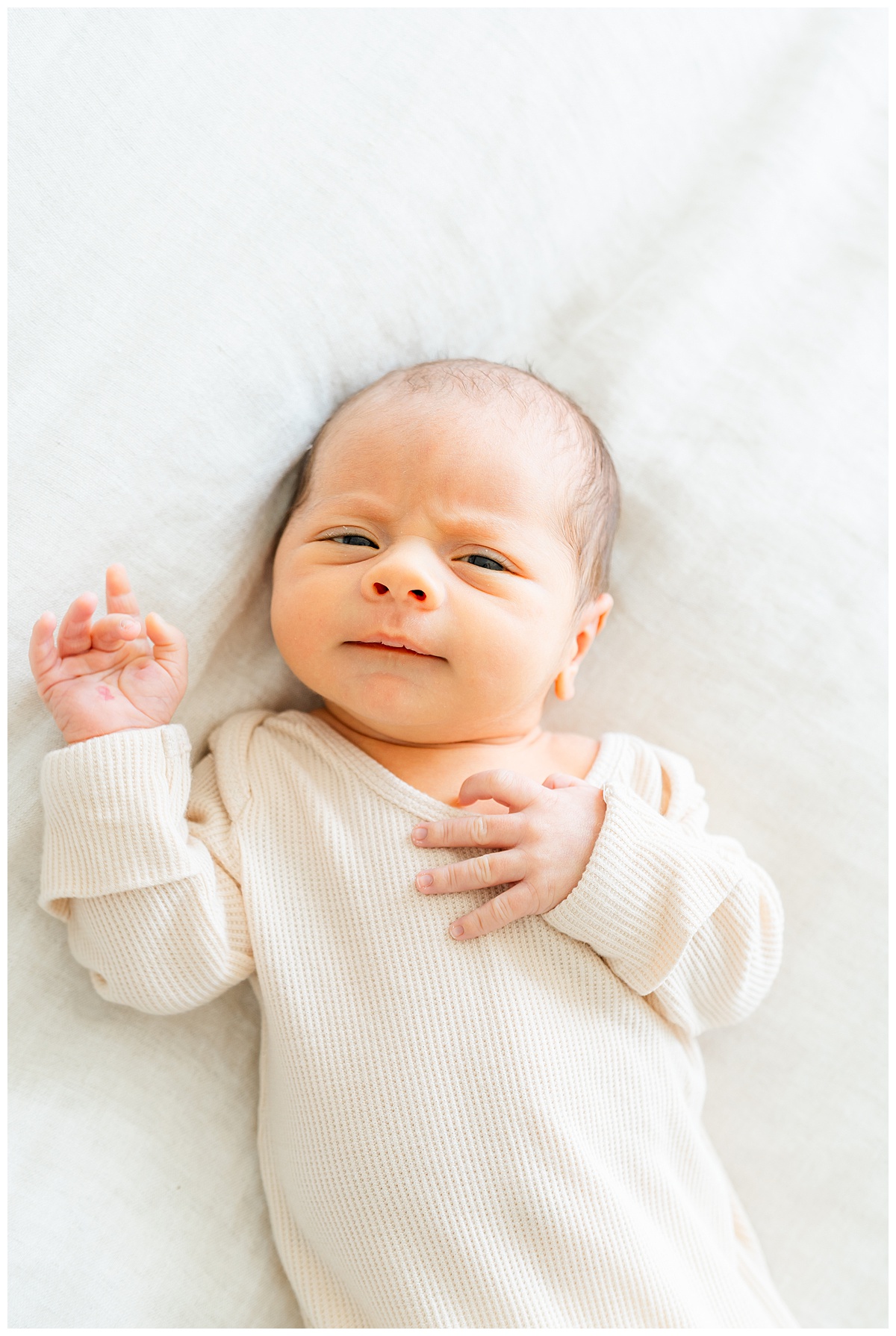 A newborn baby lays on a bed with his eyes open and looks at his Leander Photographer during his lifestyle newborn session. 