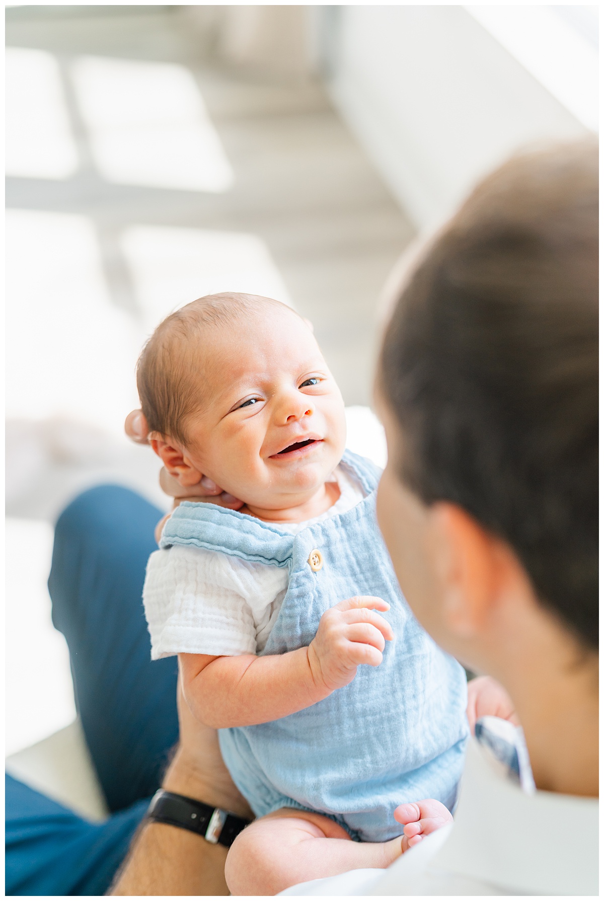 A newborn baby is held facing his father. He looks up at his father with his eyes opened and a smile, candidly captured by a Leander Photographer.