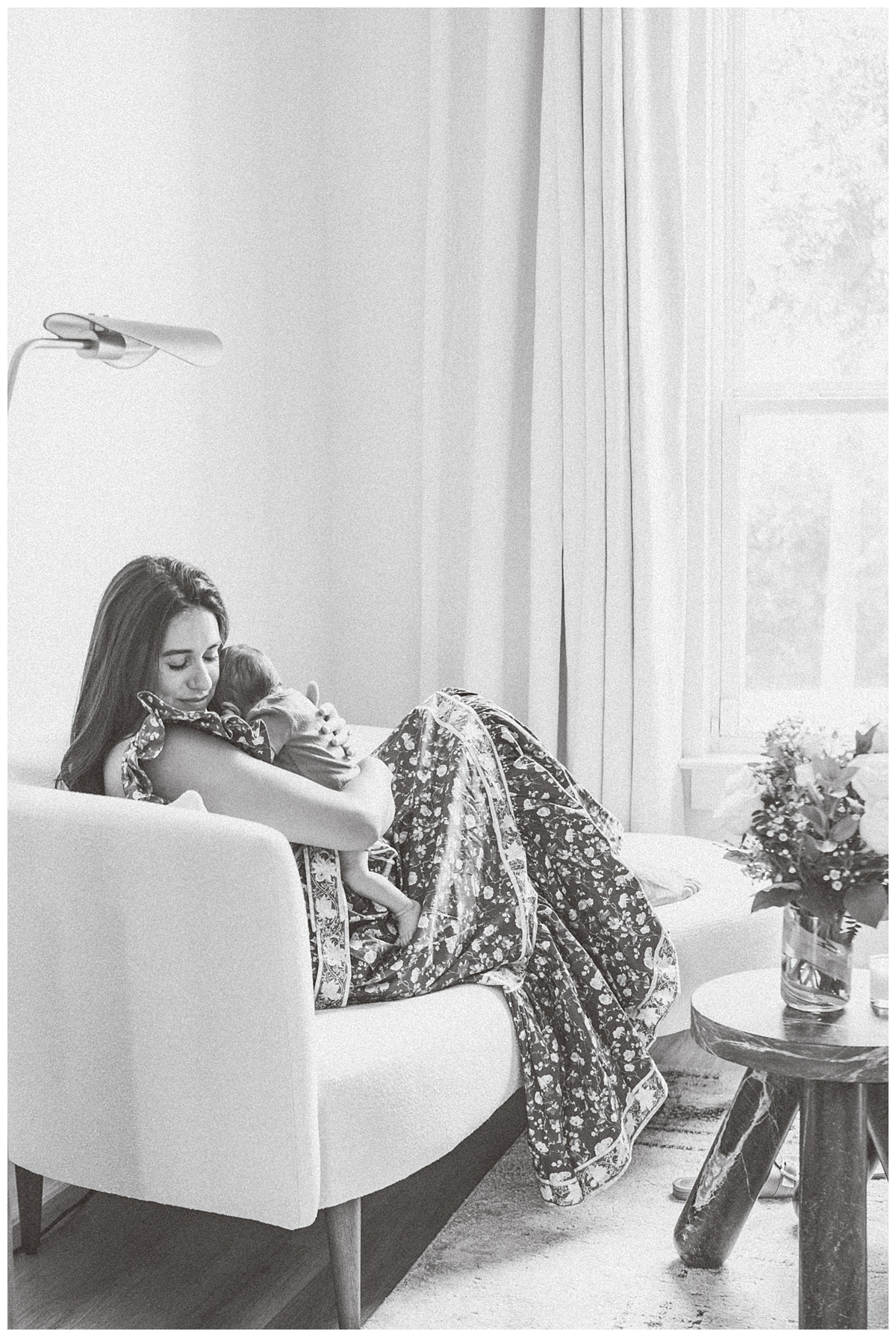 A mother sits on a daybed with her newborn baby in her arms. She closes her eyes and rests her head on her baby's head, quietly captured by a Leander Photographer.