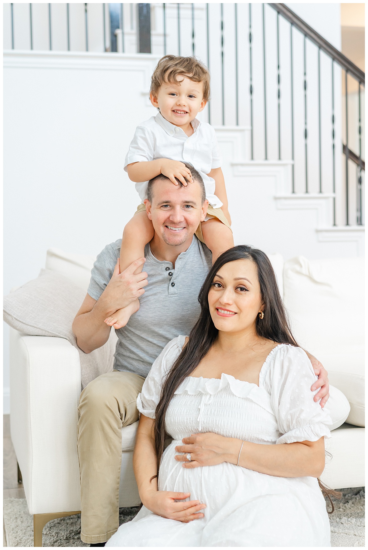 A family of three sits on a white couch during their in-home maternity model call in Leander, TX.