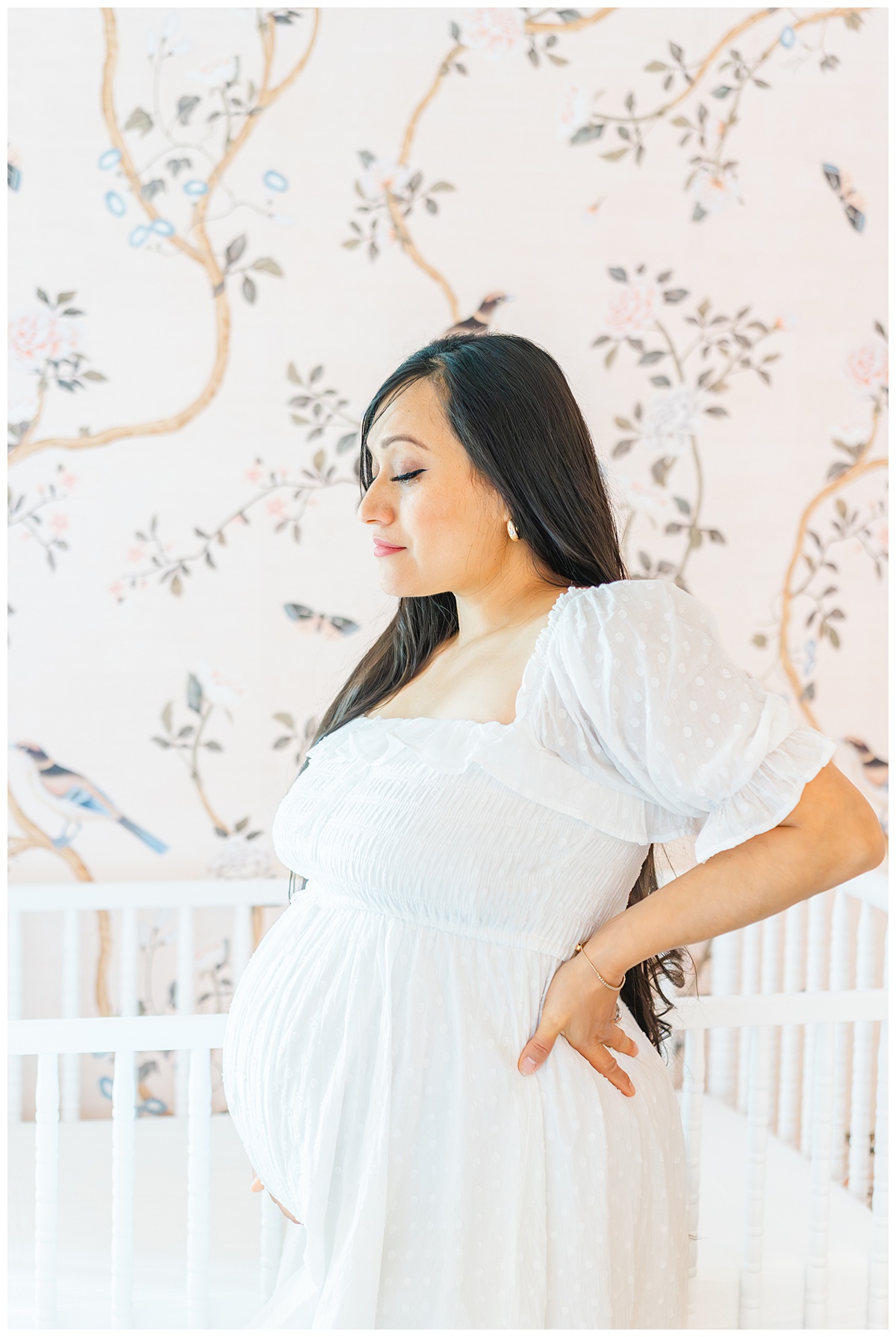 A pregnant mother stands in front of a white crib in a pink nursery, beautifully captured by a Leander Maternity Photographer.