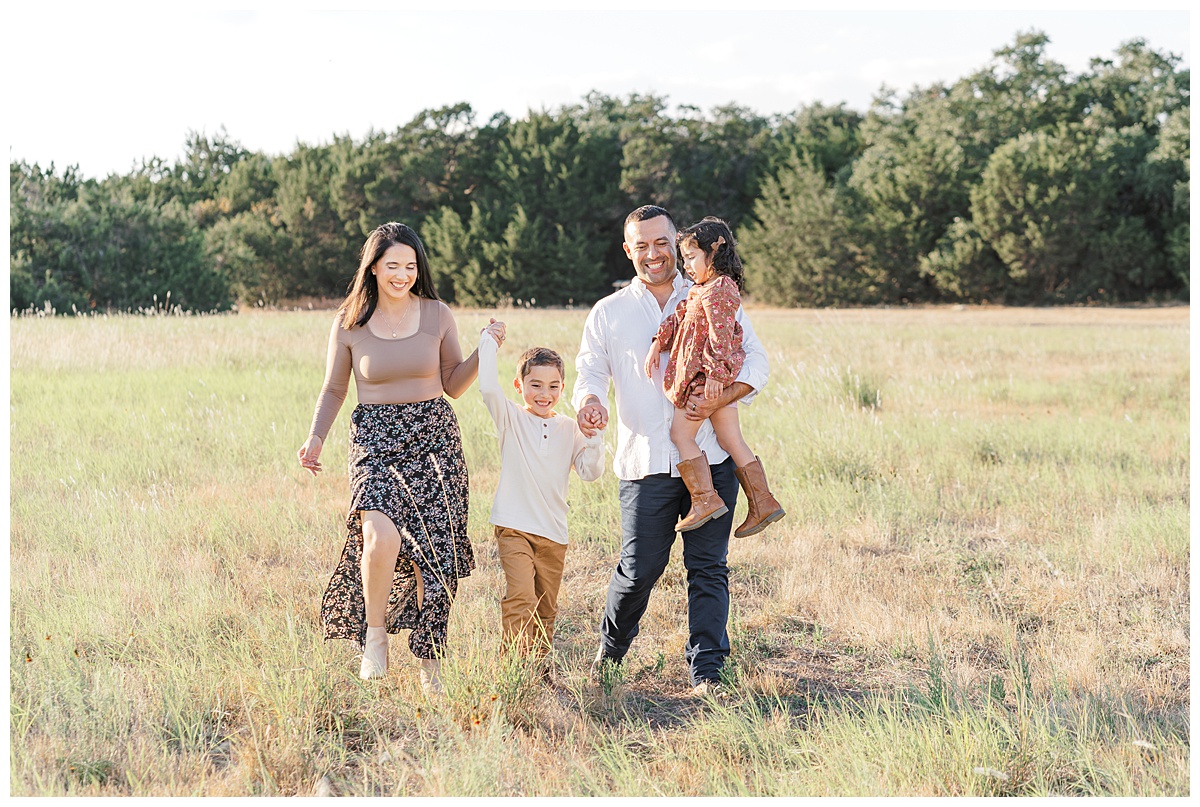 Best Photo Locations In Austin | A family of 4 walks in the tall grass at Brushy Creek Lake Park. They hold hands and smile. 