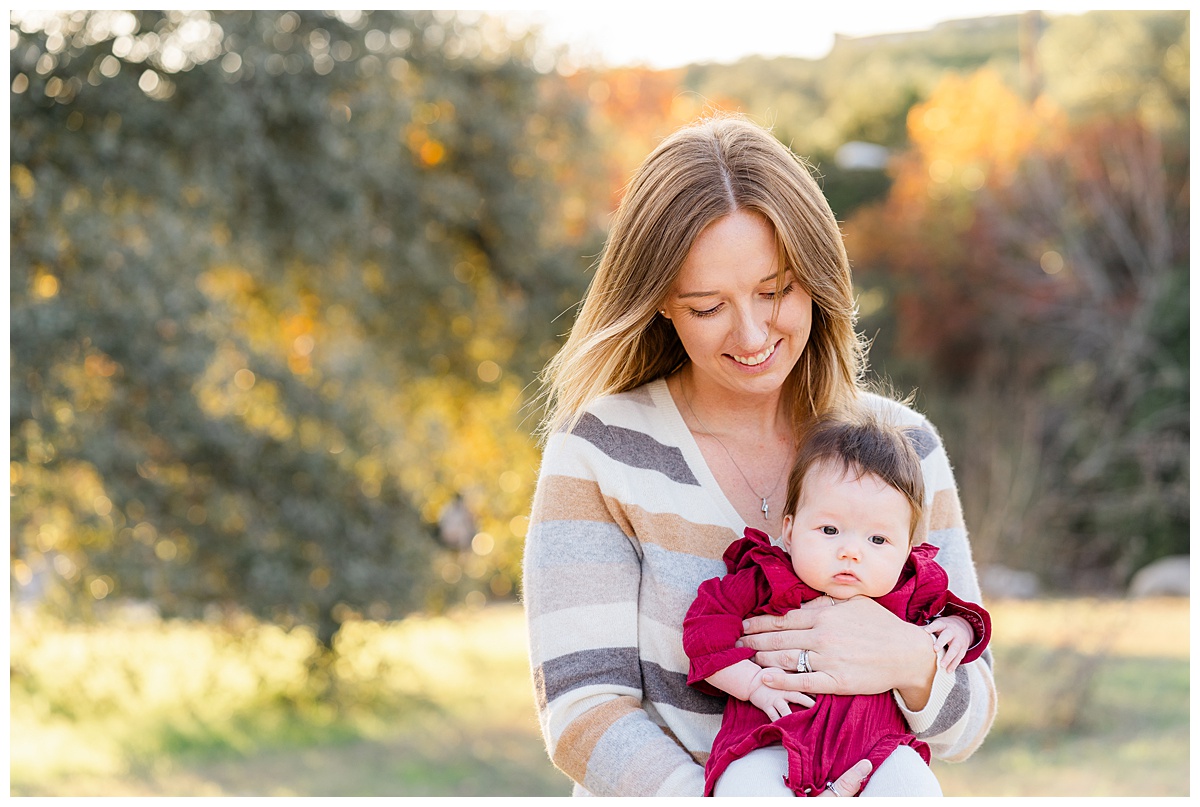 Best Photo Location in Austin | Bull Creek District Park. A mother holds her baby girl dressed in a red romper. She looks down at her and smiles.