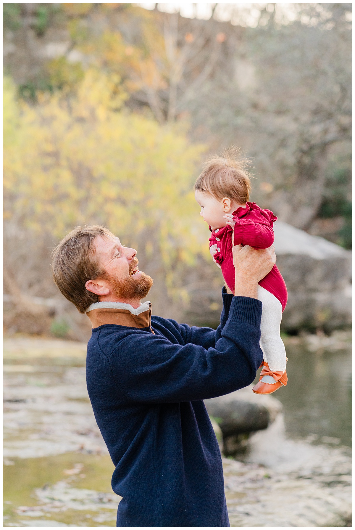 Best Photo Location in Austin | A father stands in front of the water at Bull Creek District Park. He lifts his baby girl up in the air and smiles at her.