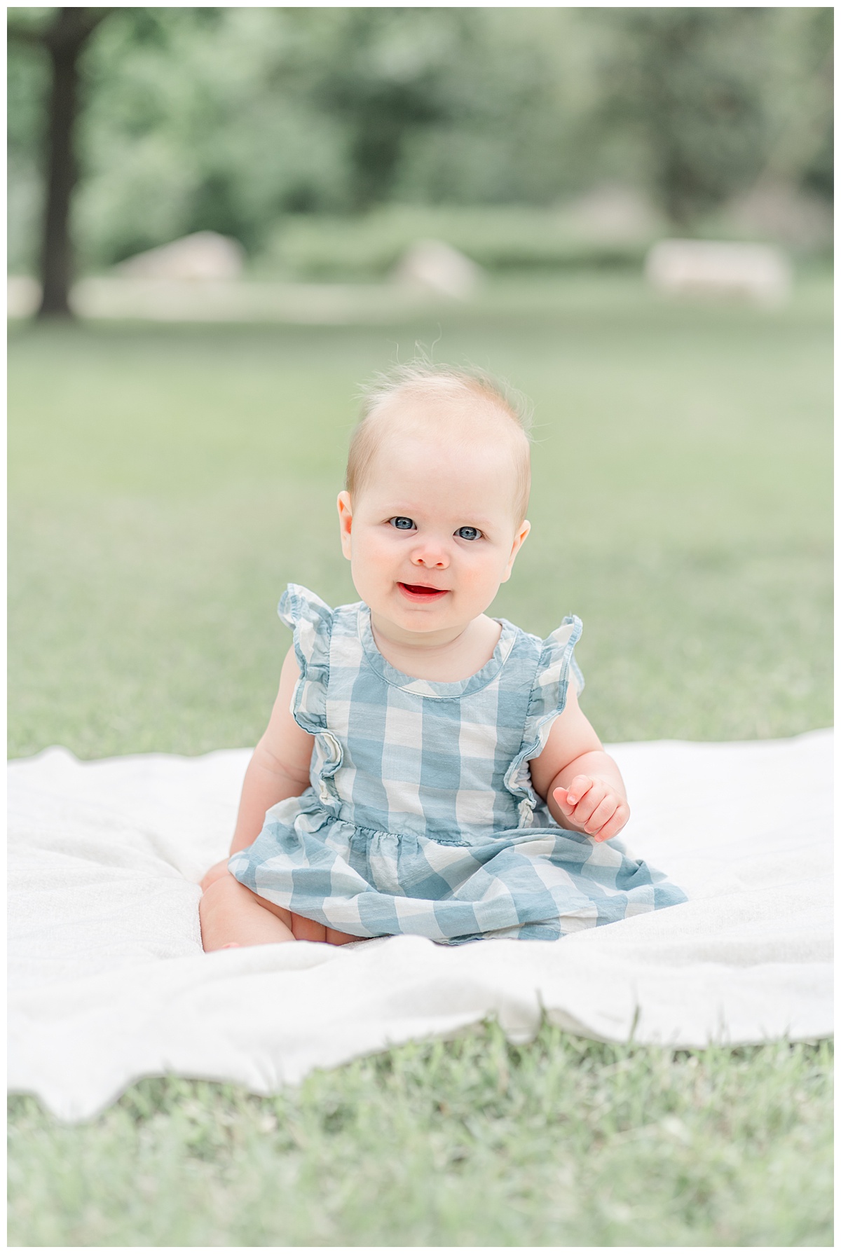 Austin Baby Photography | Baby girl sitting in the grass on a white blanket smiling at the camera during her milestone photo session.