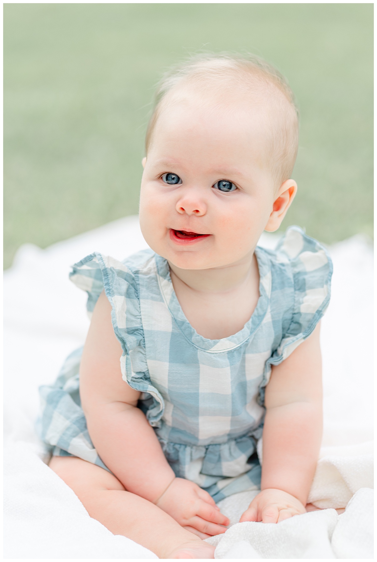 Austin Baby Photography | Close-up of a 6-month baby girl dressed in a blue gingham dress with bright blue eyes and smiling. 