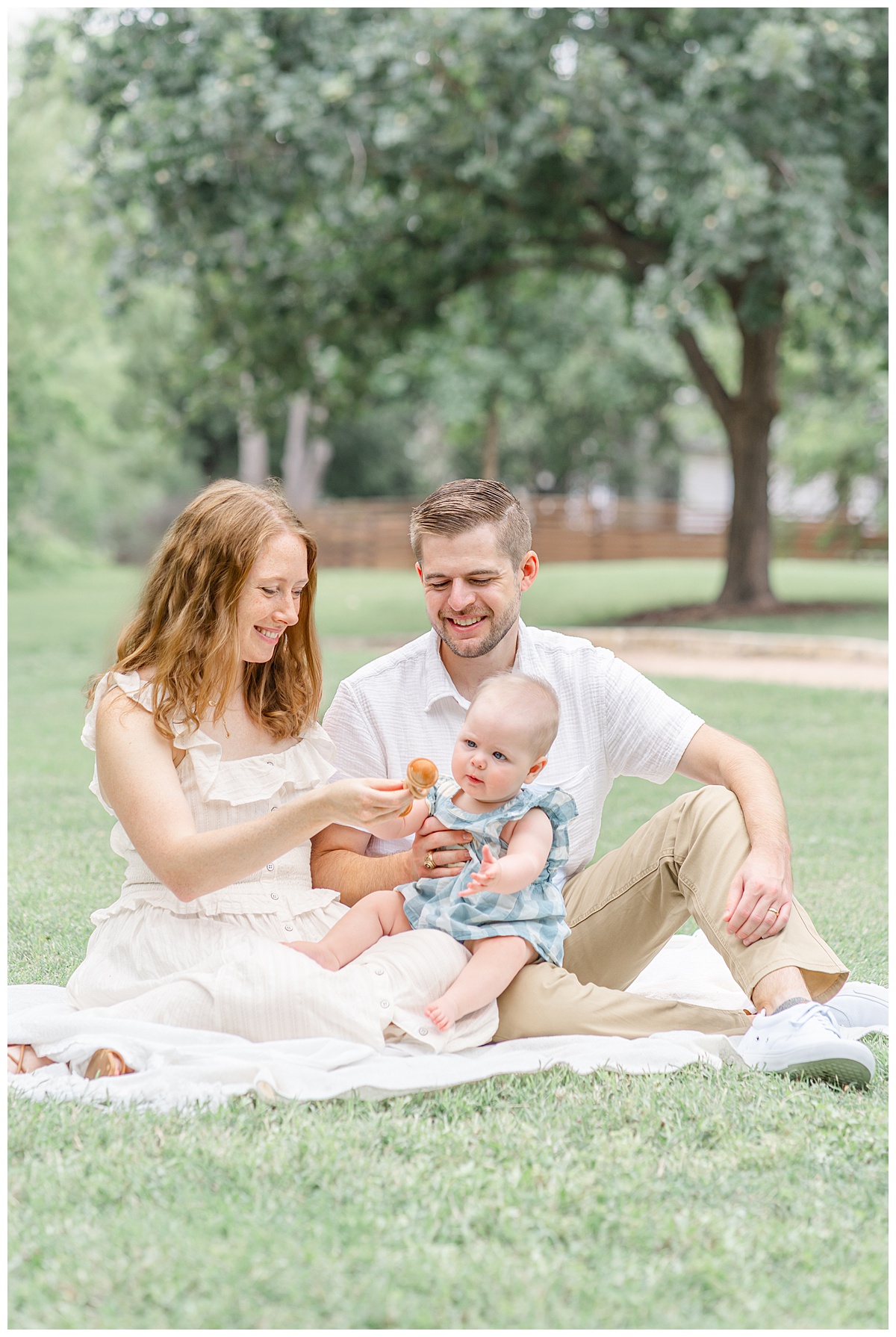 A family of 3 sits on a blanket at Katherine Fleischer Park. The mom and dad play with their baby girl. They smile together in this candid shot captured by a family photographer in Austin, TX.