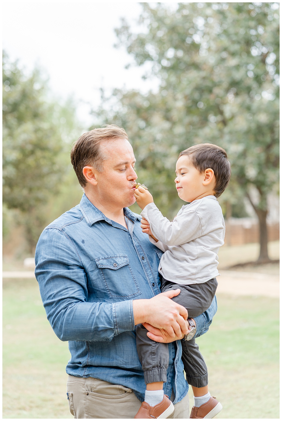A father holds his young son in his arms and kisses a flower the son hands him during their family photos in Austin.