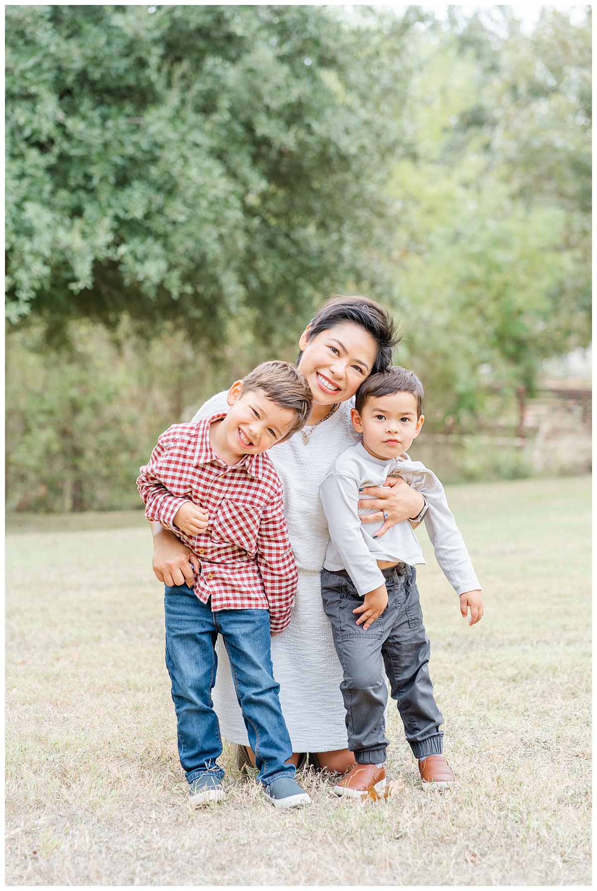 a mother dressed in a white dress bends down to her two young boys for their photos with their dog at Katherine Fleischer Park.