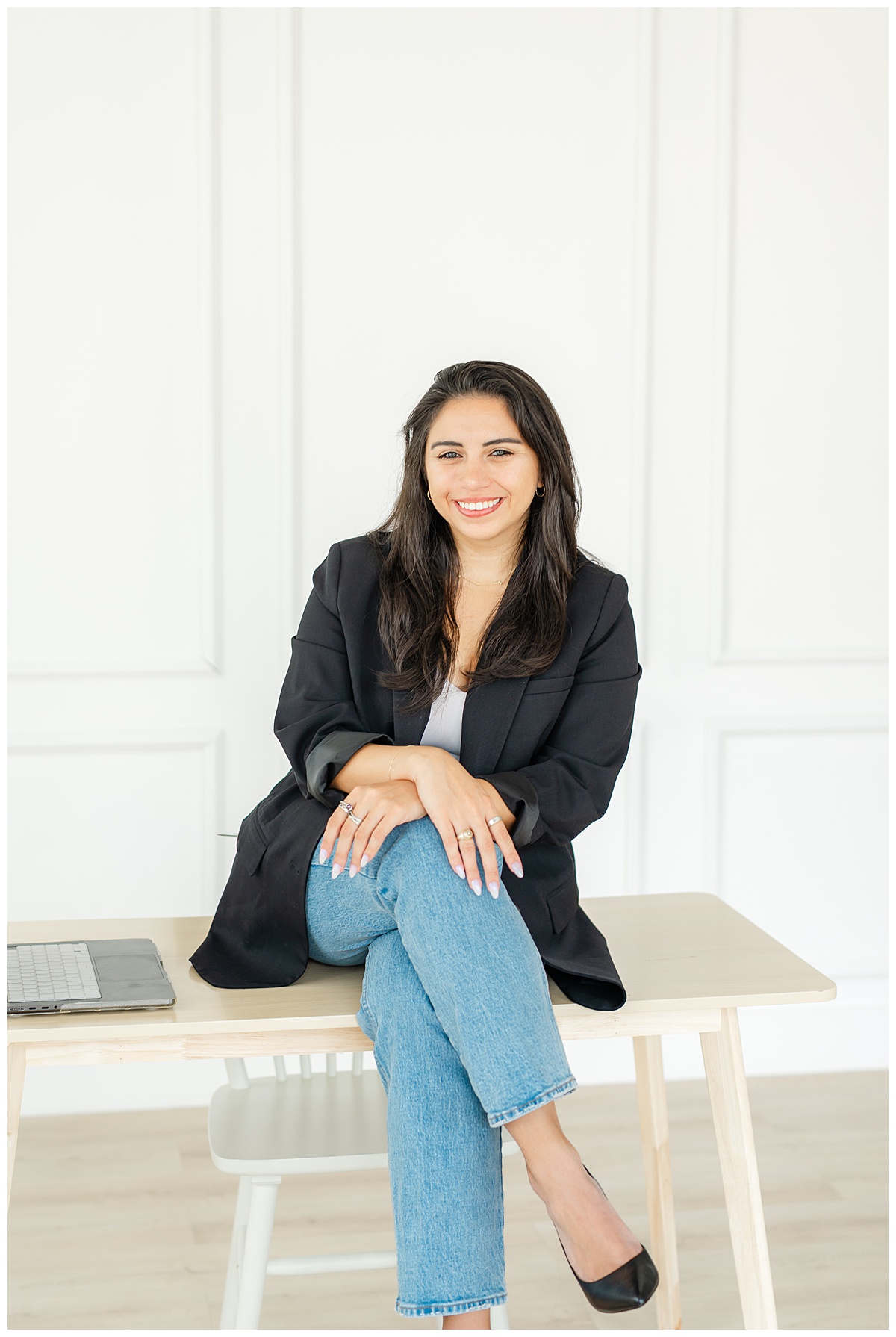 a woman sits on a desk with her legs crossed and smiles at her Austin photographer during her branding session.