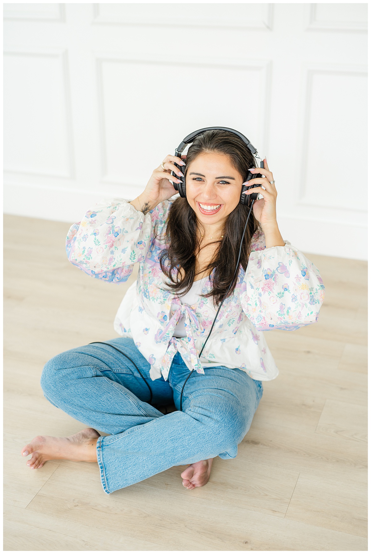 a woman sits on the floor of an Austin photo studio with a headset on her head and smiles. 