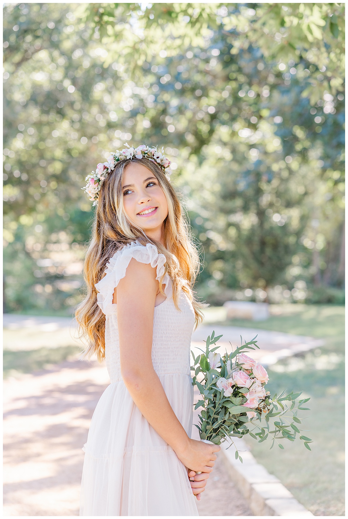A teenage girl with long blond hair holds a bouquet and looks over her shoulder with a smile - captured by an Austin family photographer.