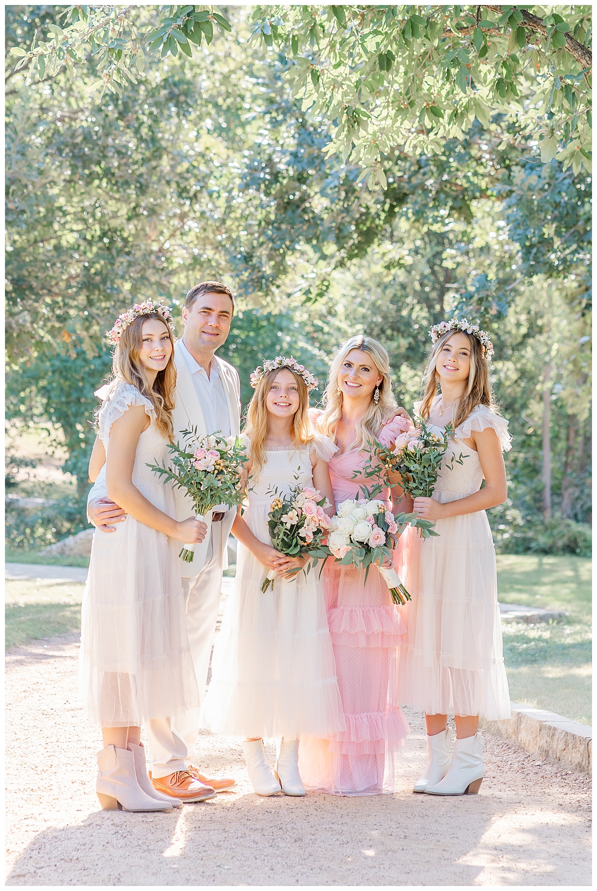 a family stands under a tree. The mother and her three daughters hold bouquets during their anniversary family photos at an Austin park. 