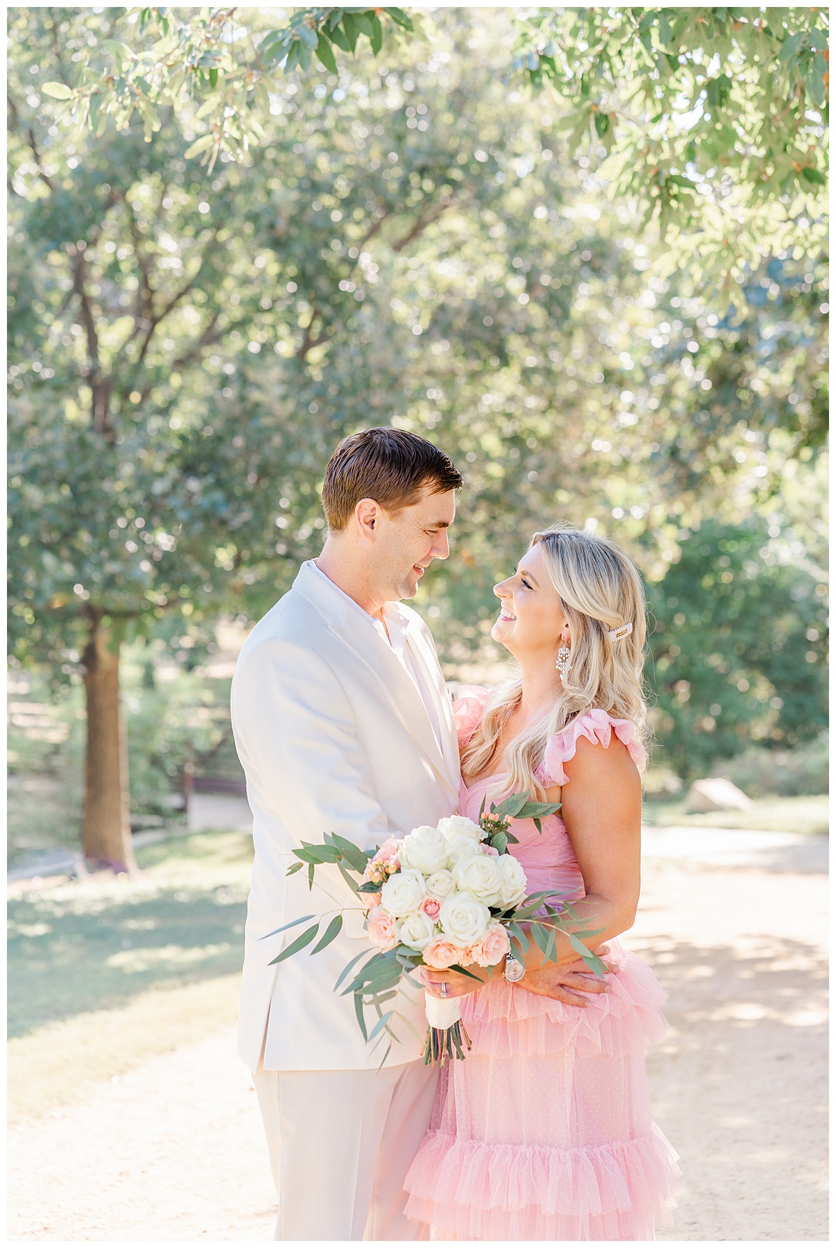 A couple stands facing each other and smiling for their anniversary photos in Austin, TX. The woman wears a long pink dress and holds a bouquet. 