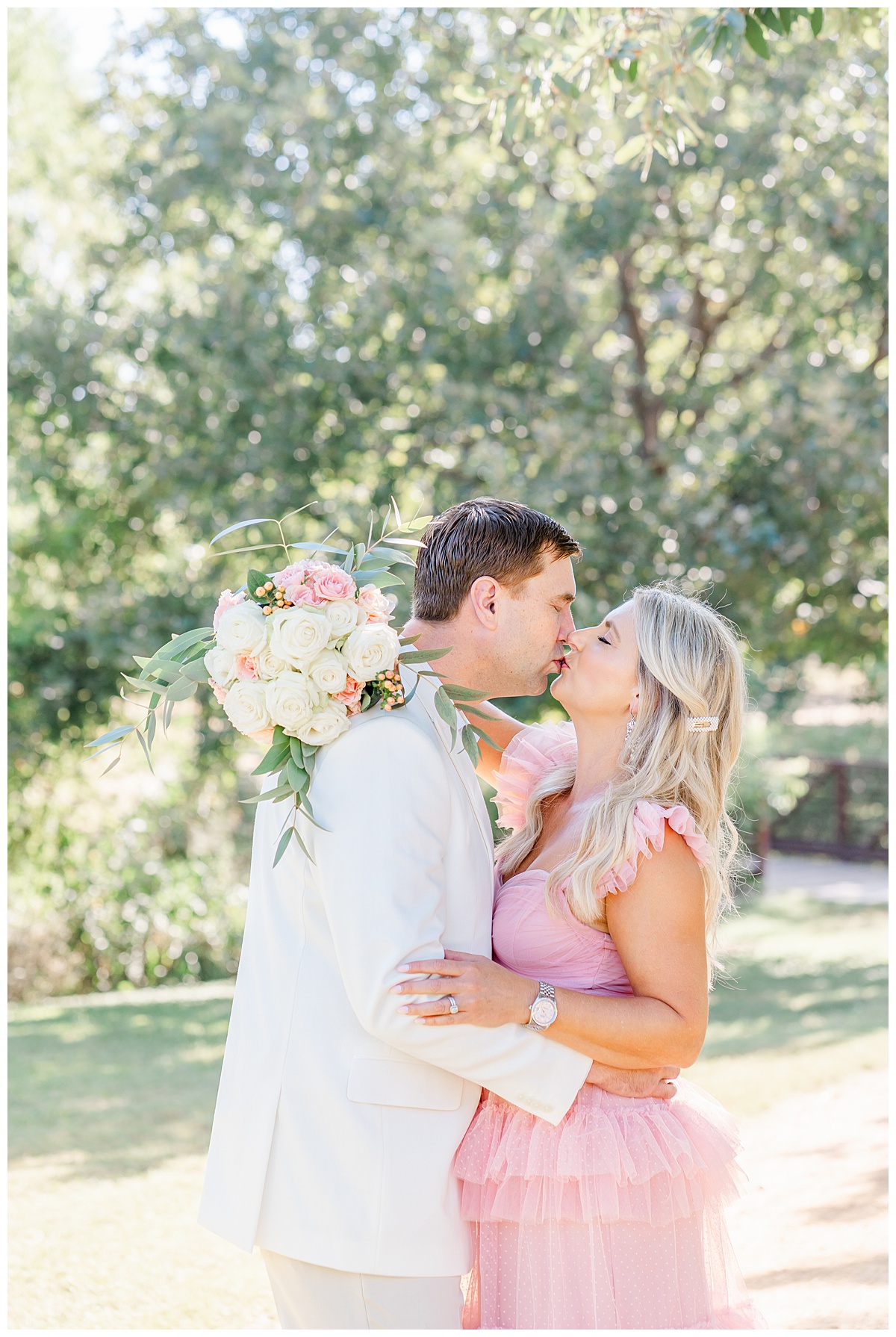 a woman dressed in a long pink dress kisses her husband while wrapping her arm around his neck and holding a bouquet for their anniversary pictures in Austin. 