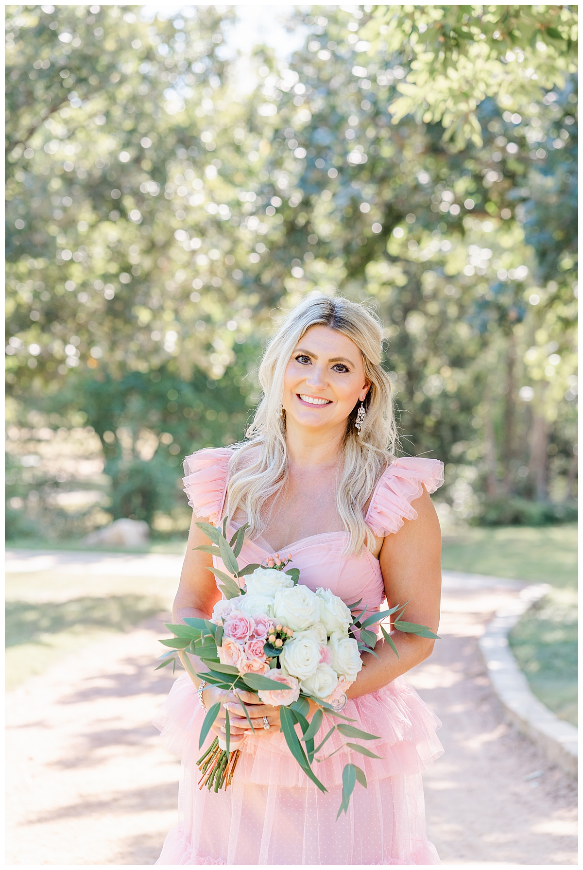 A woman with long blond hair holding a bouquet poses and smiles for her anniversary family photos at Katherine Fleischer Park - captured by an Austin family photographer.