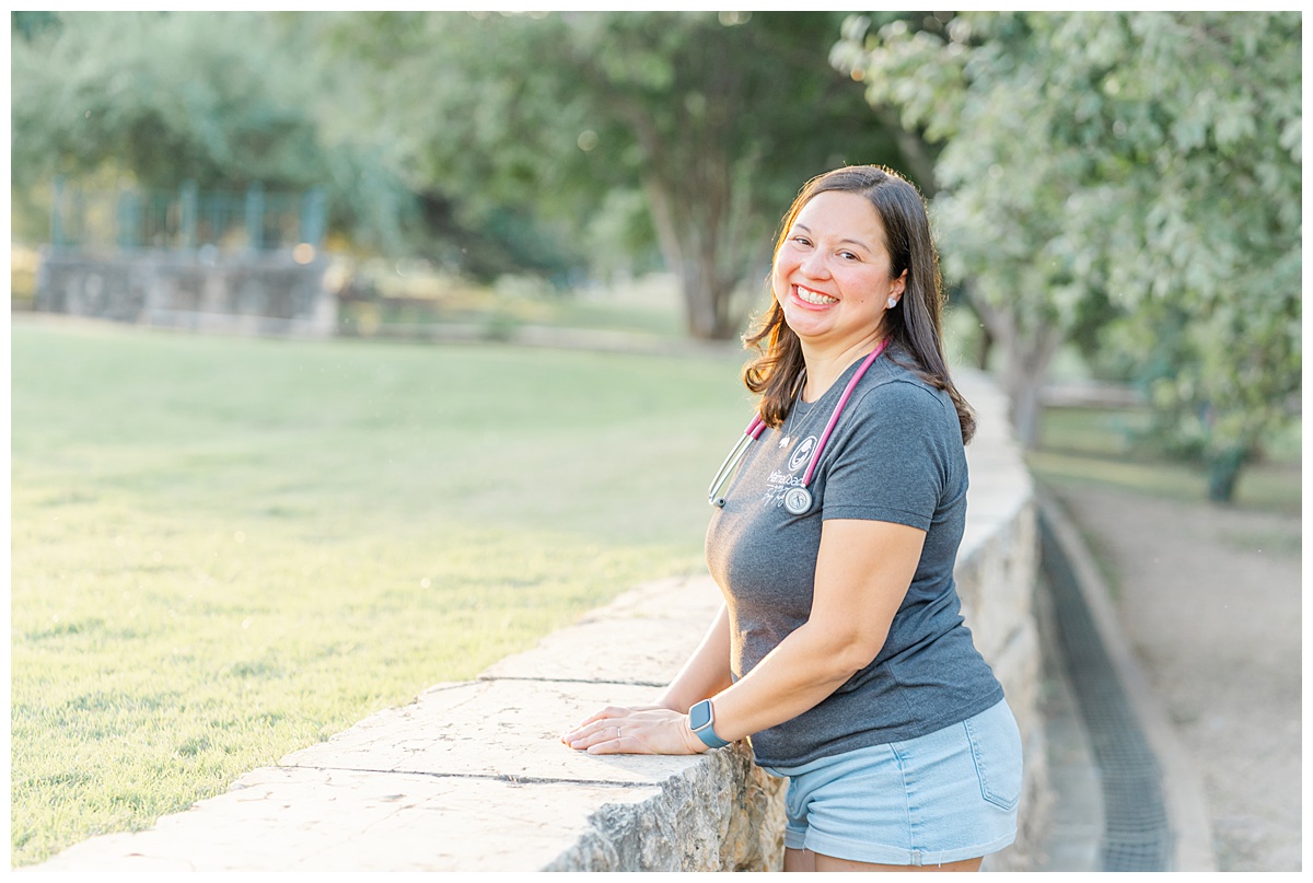 Emily Tavag - Austin Mama Coach - leans against a half wall at Butler Metro Park during her headshot session with an Austin newborn & family photographer.