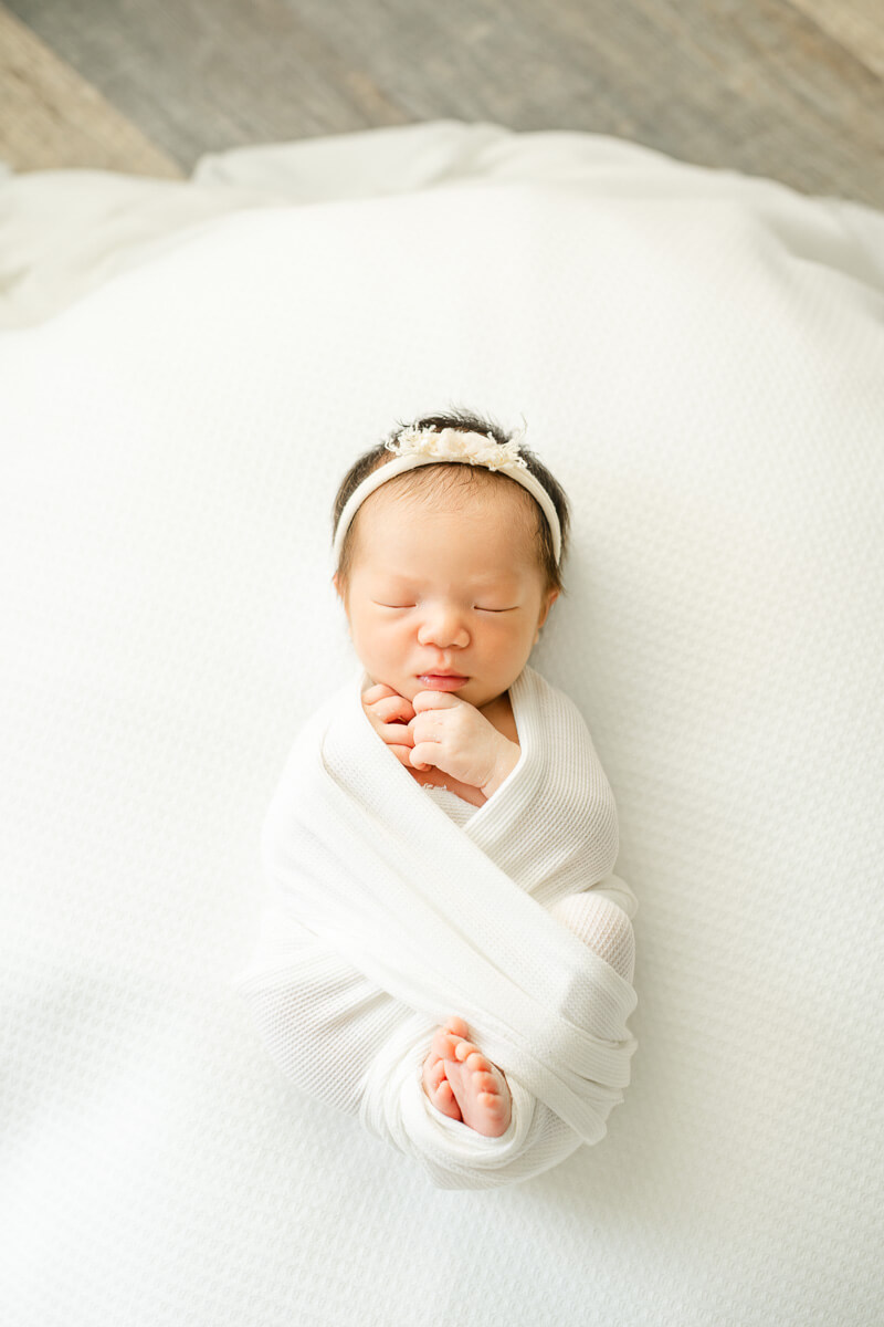newborn baby girl lays on white bean bag while sleeping.