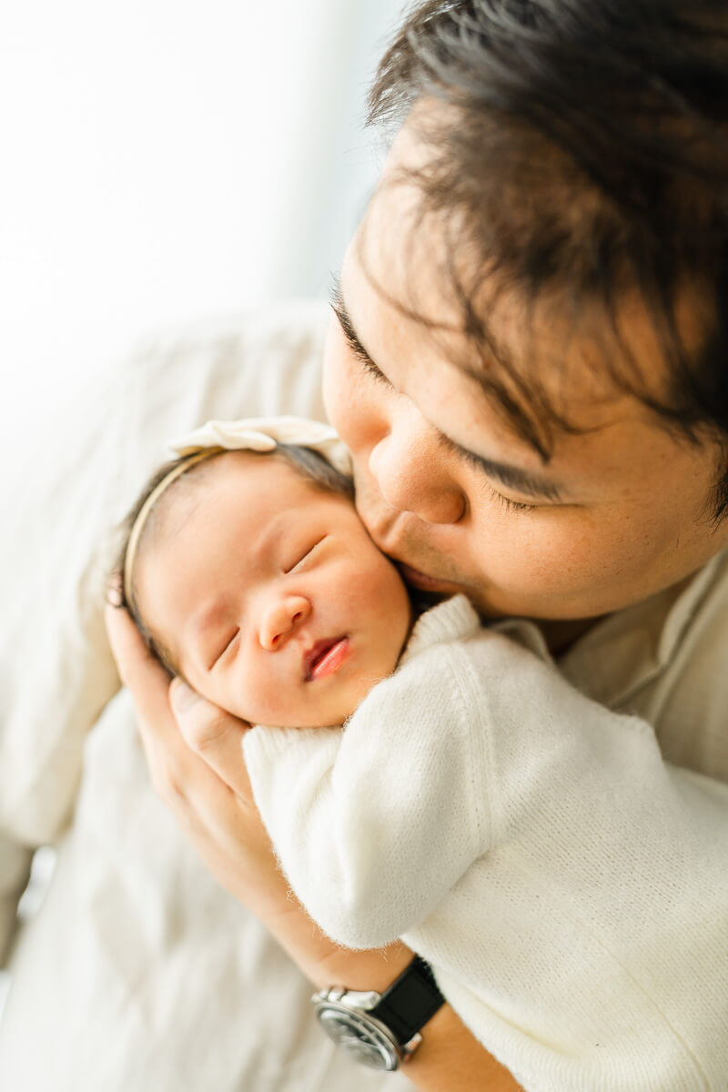 father kisses baby on cheek during lifestyle newborn session in Austin. 