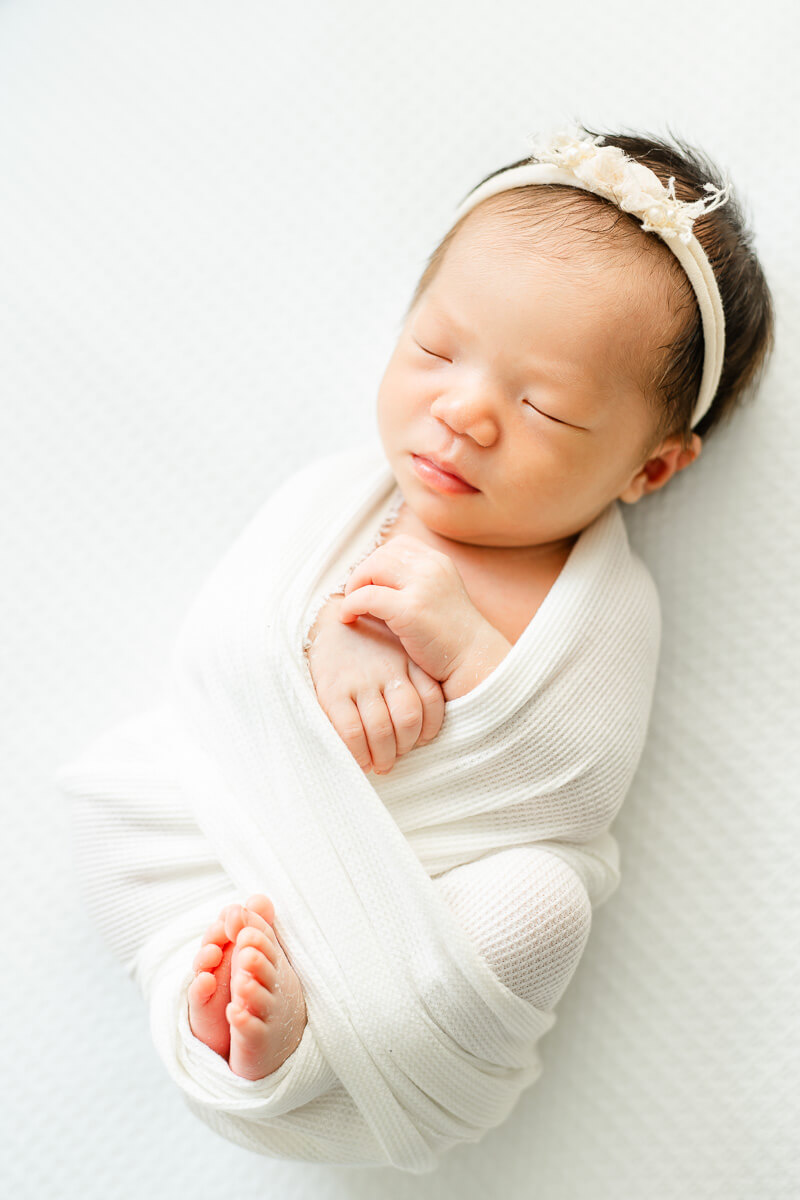 sleeping infant girl wrapped in blanket and laying on white sheet.